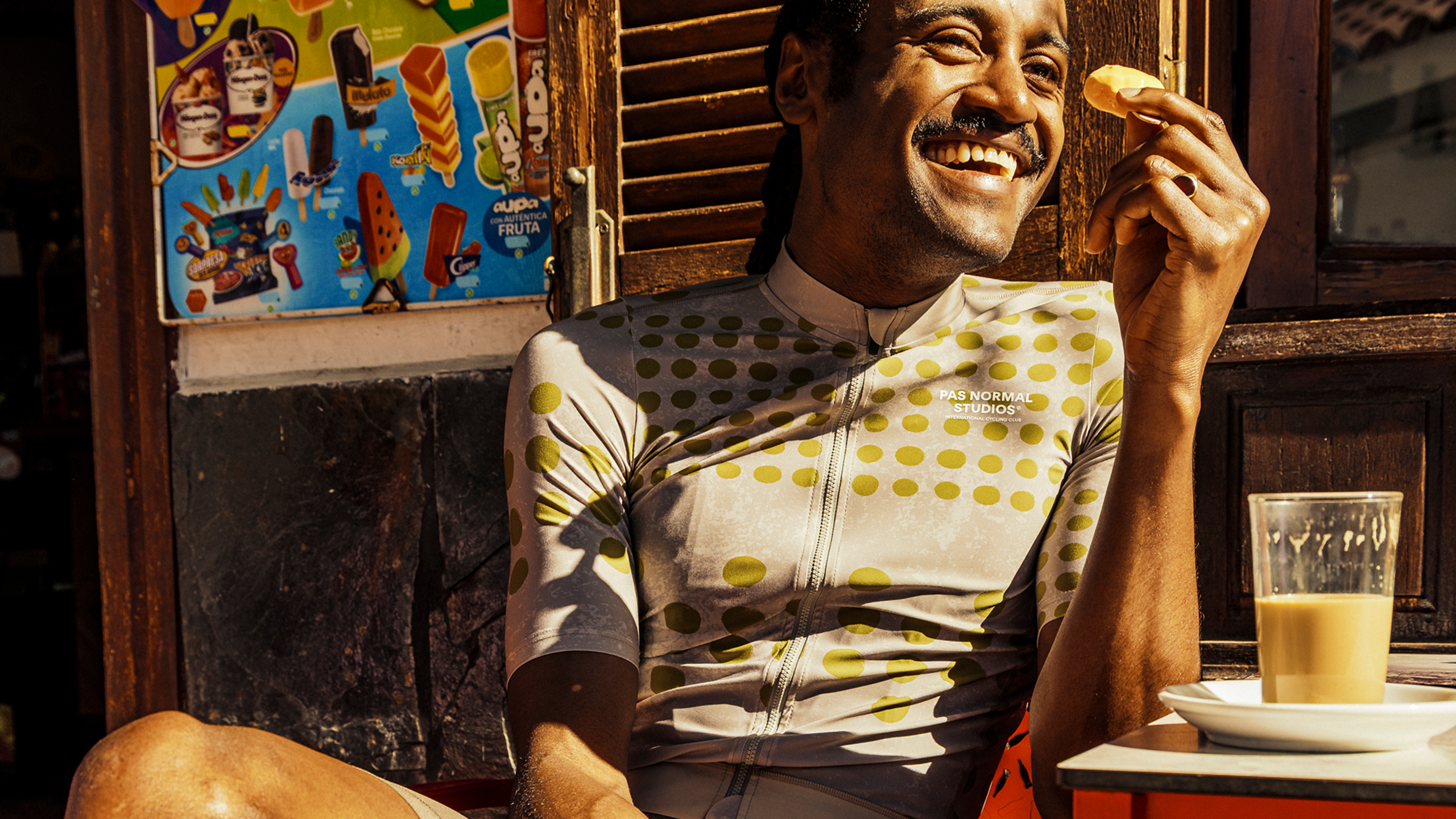 Model wearing Men's Mechanism Jersey in white with yellow polka dot pattern, eating at outdoor cafe