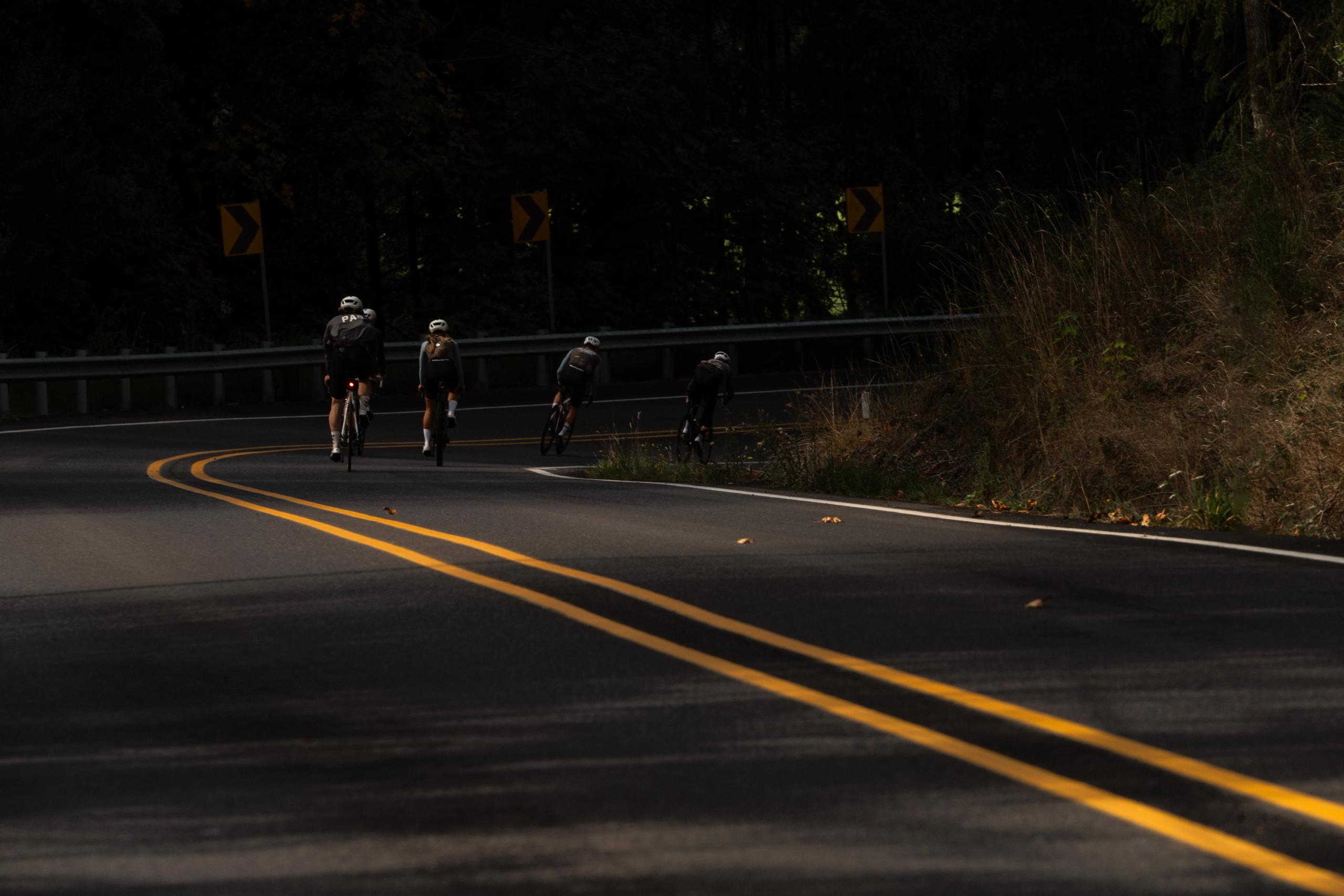 Four cyclists riding on winding mountain road with guardrail and yellow lines