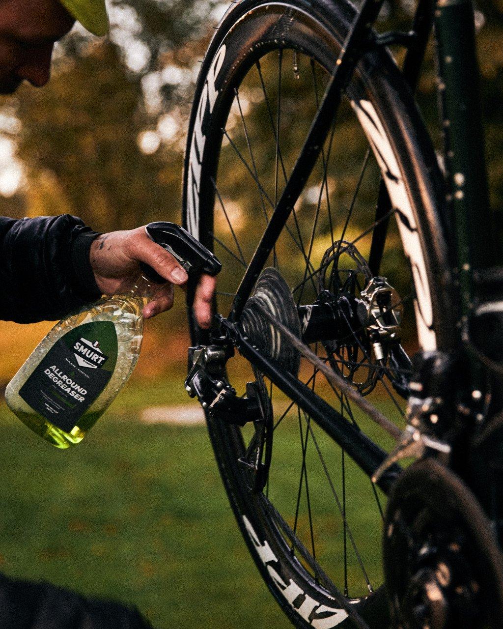 Hand spraying bike degreaser on bicycle wheel and disc brake components outdoors