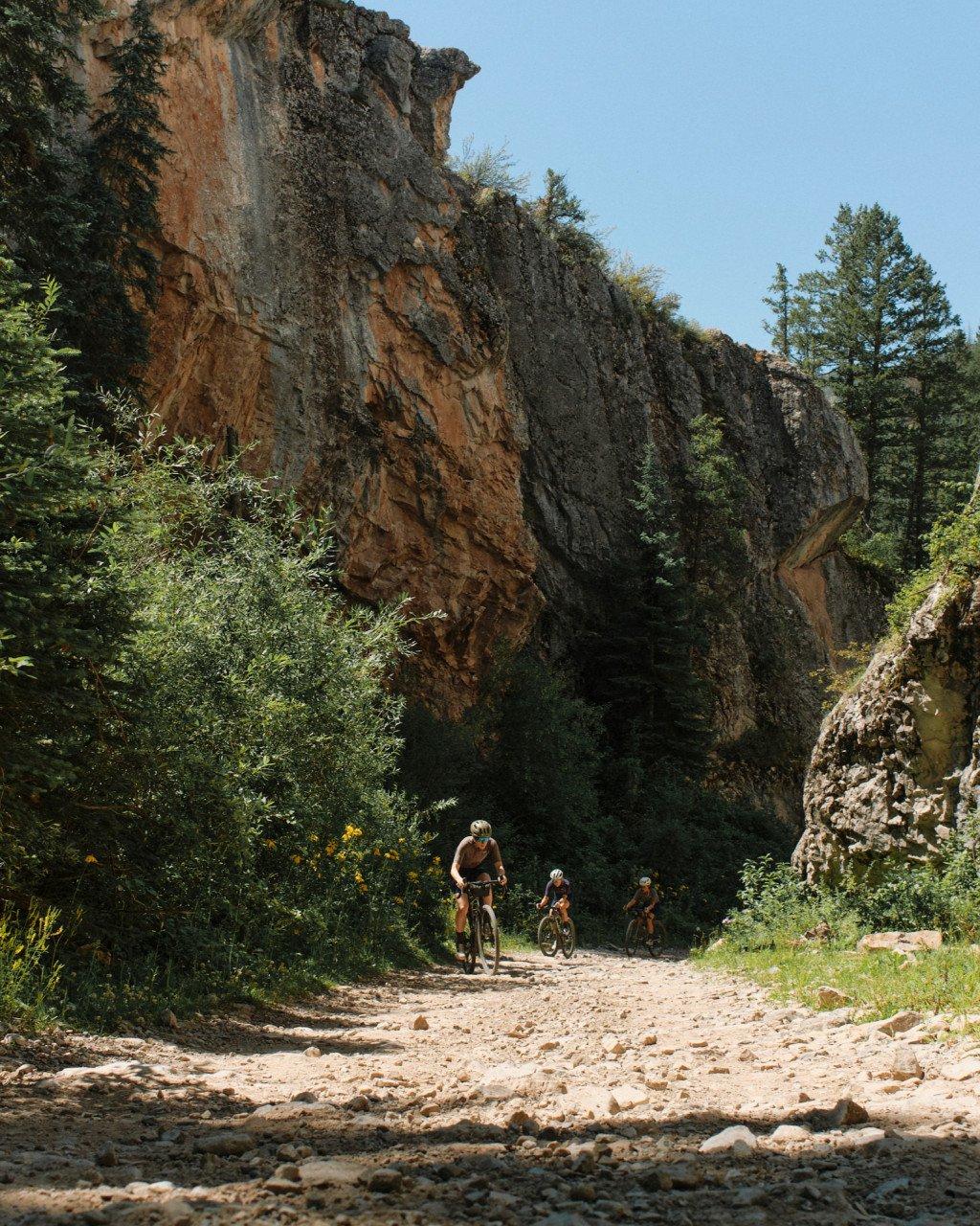 Three cyclists riding gravel bikes on rocky trail through canyon with towering rock formations