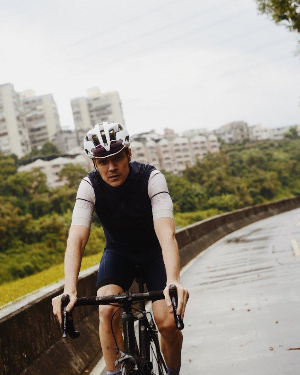 Model wearing dark navy cycling kit with white helmet on urban road