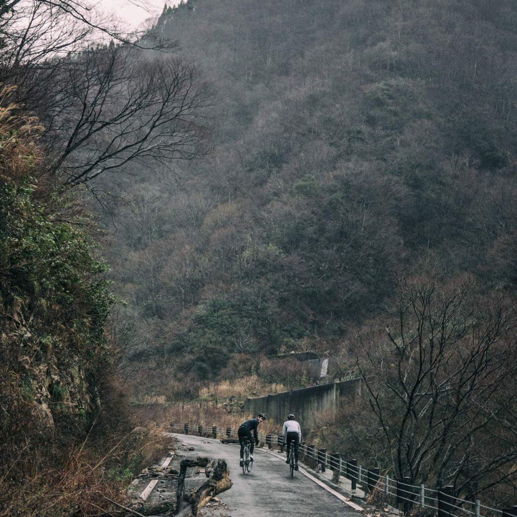 Two cyclists riding across mountain bridge in autumn landscape