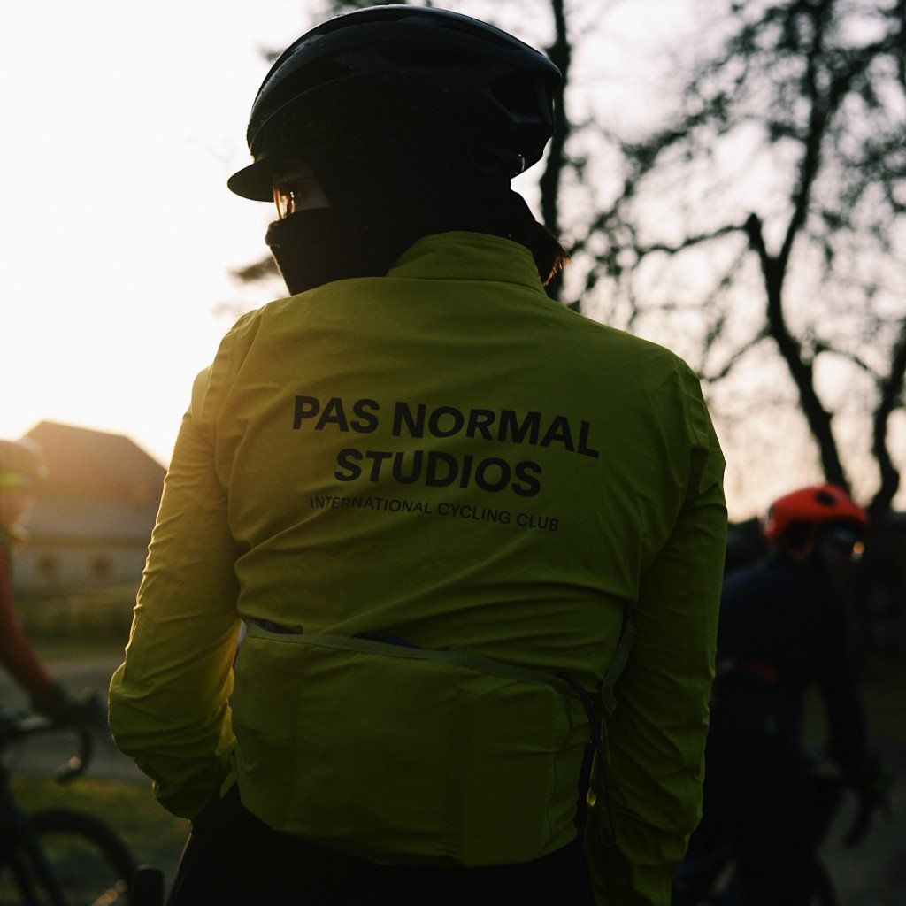 Model wearing green cycling jacket with back branding, black helmet, outdoors at sunset