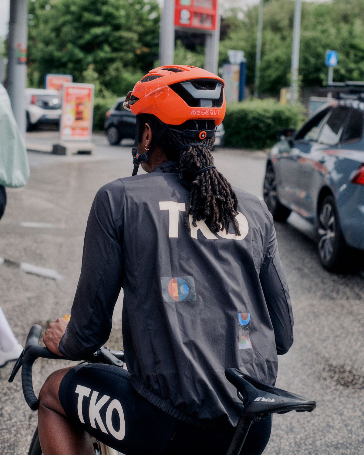 Model wearing Men's TKO long sleeve jersey in dark grey with graphic design elements, orange helmet, on bike