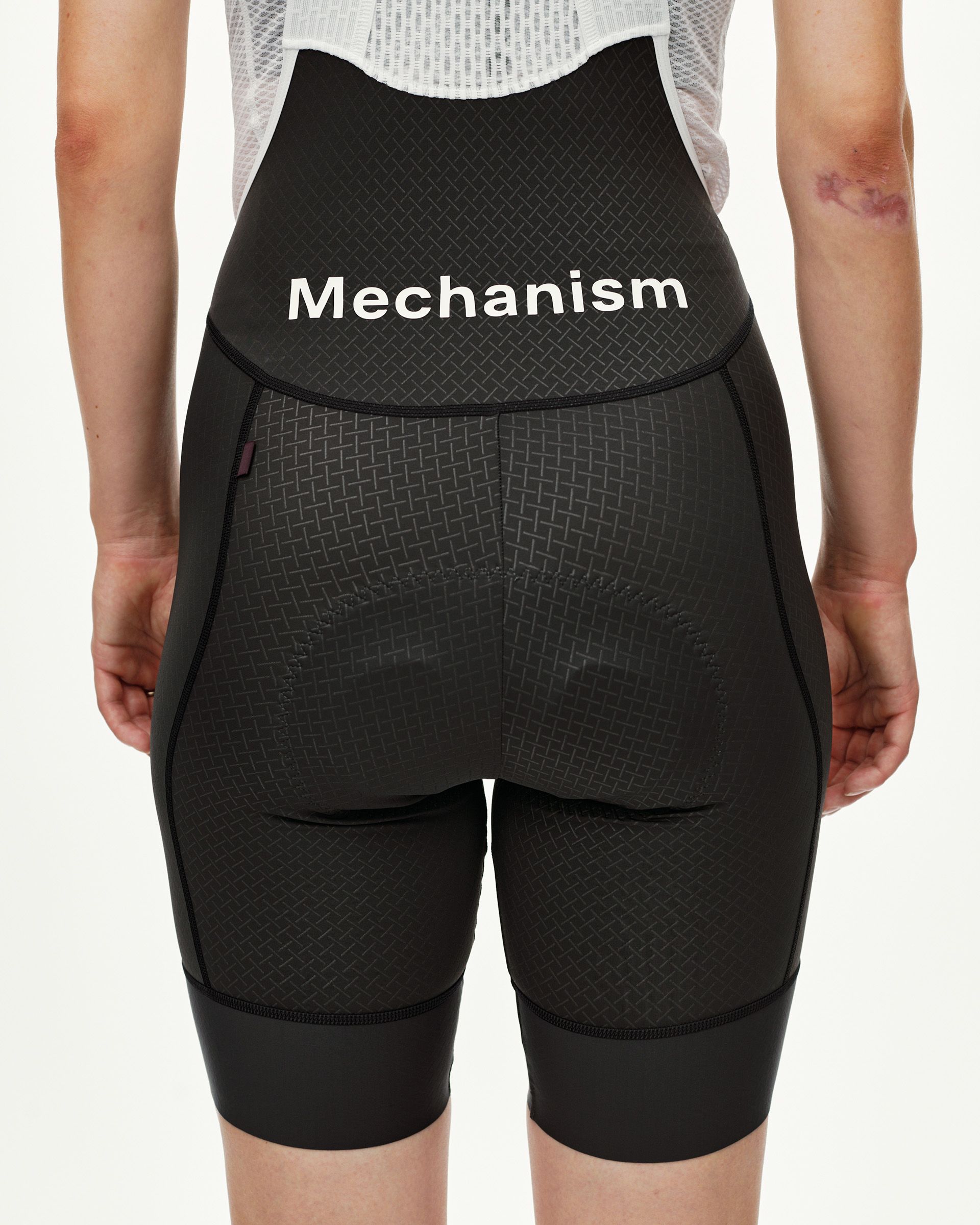 Black Mechanism cycling bibs on model, rear view with white waistband text and woven texture panel