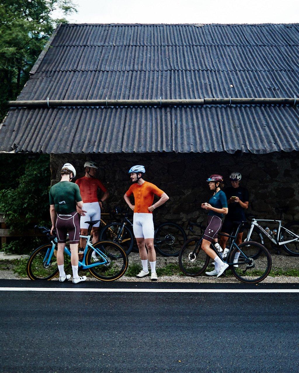 Group of cyclists in colorful jerseys with bikes during road stop near rural building