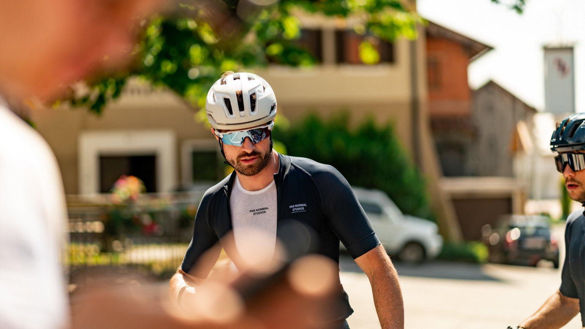 Model wearing white mesh base layer under dark cycling jersey with helmet and sunglasses in urban setting