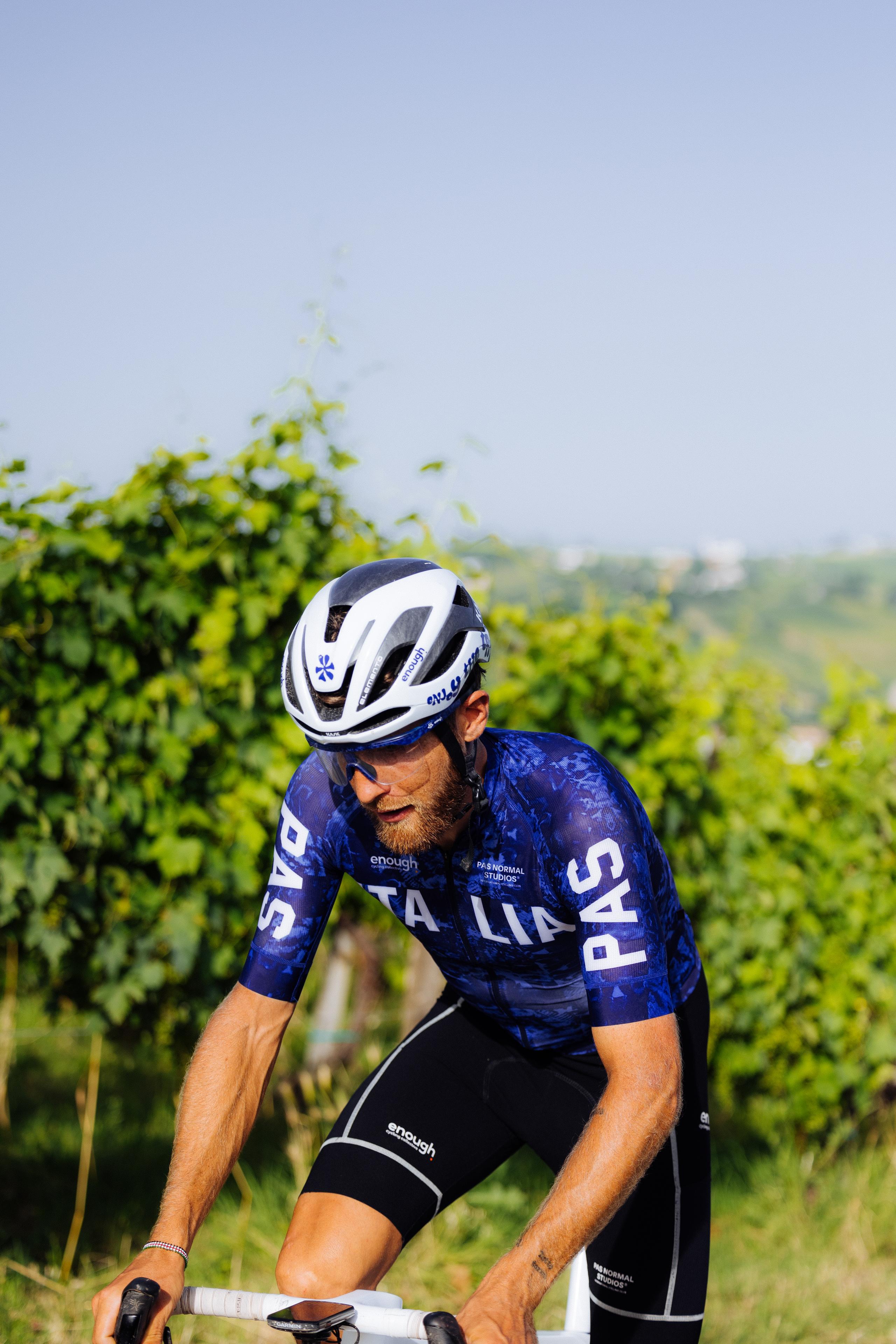 Model wearing blue patterned short sleeve cycling jersey and black shorts in aerodynamic position outdoors