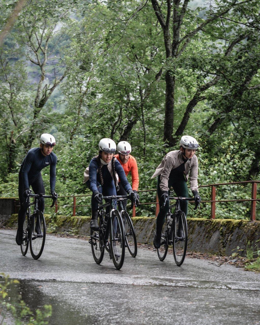 Four cyclists in aerodynamic position on time trial bikes riding through forested road in Norway