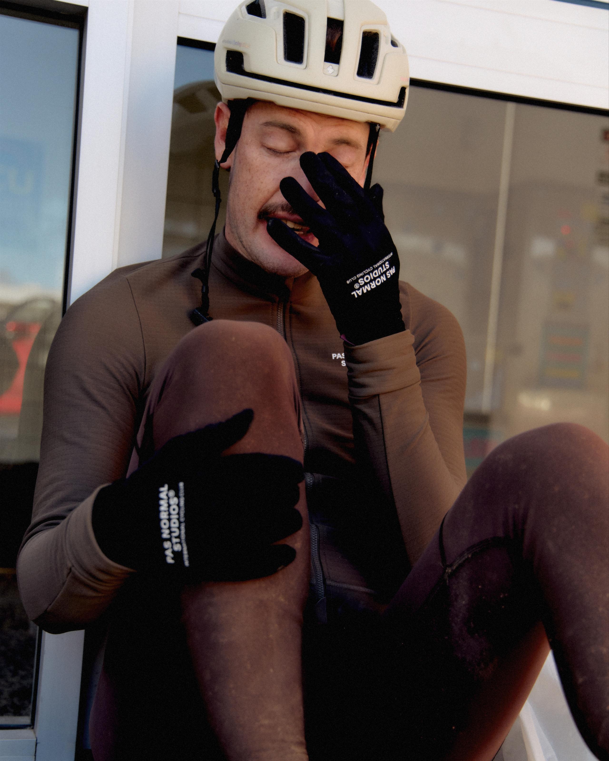 Model wearing brown long sleeve jersey and black cycling gloves, adjusting helmet in indoor setting