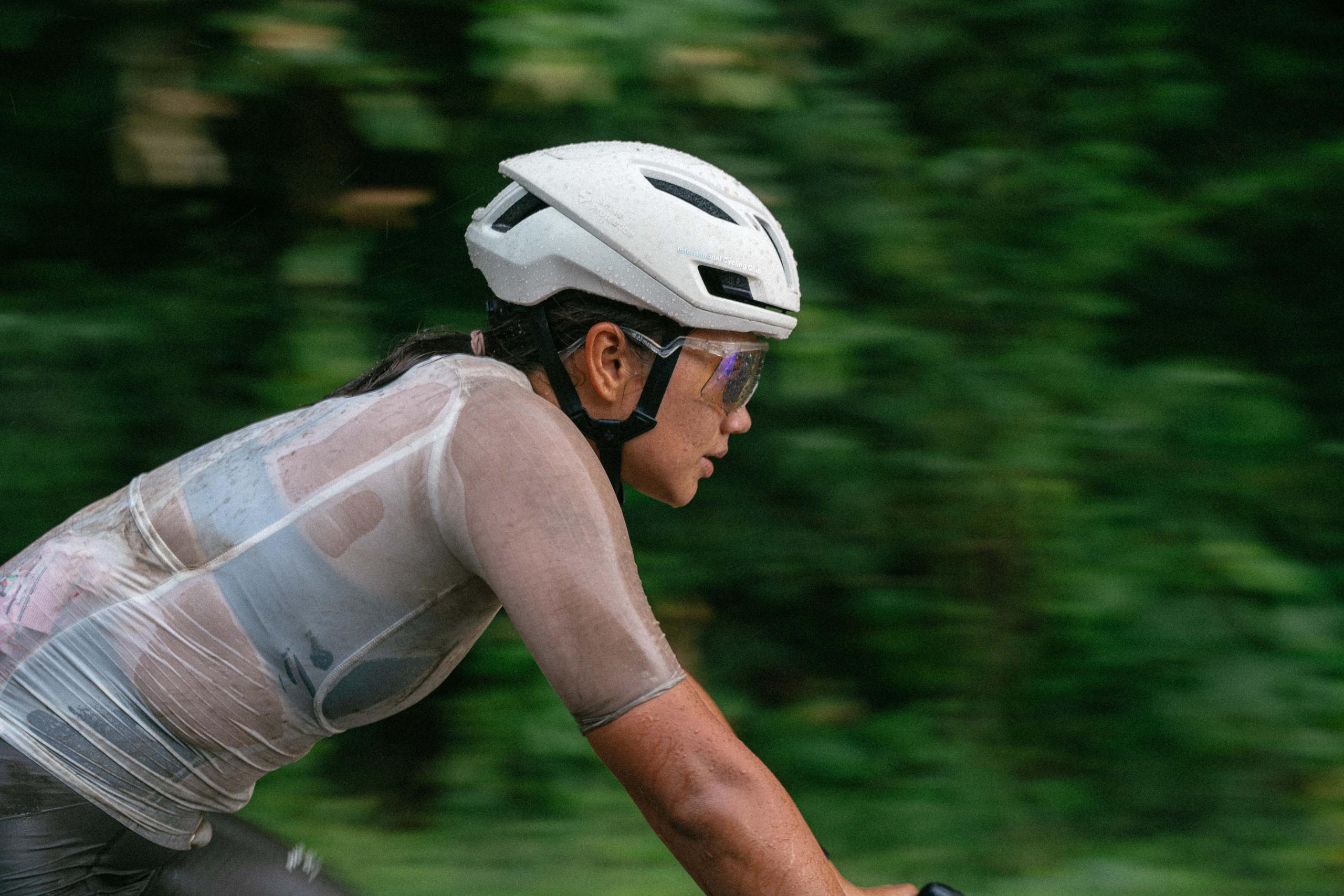 Model wearing transparent cycling jacket and white helmet in aerodynamic position on road