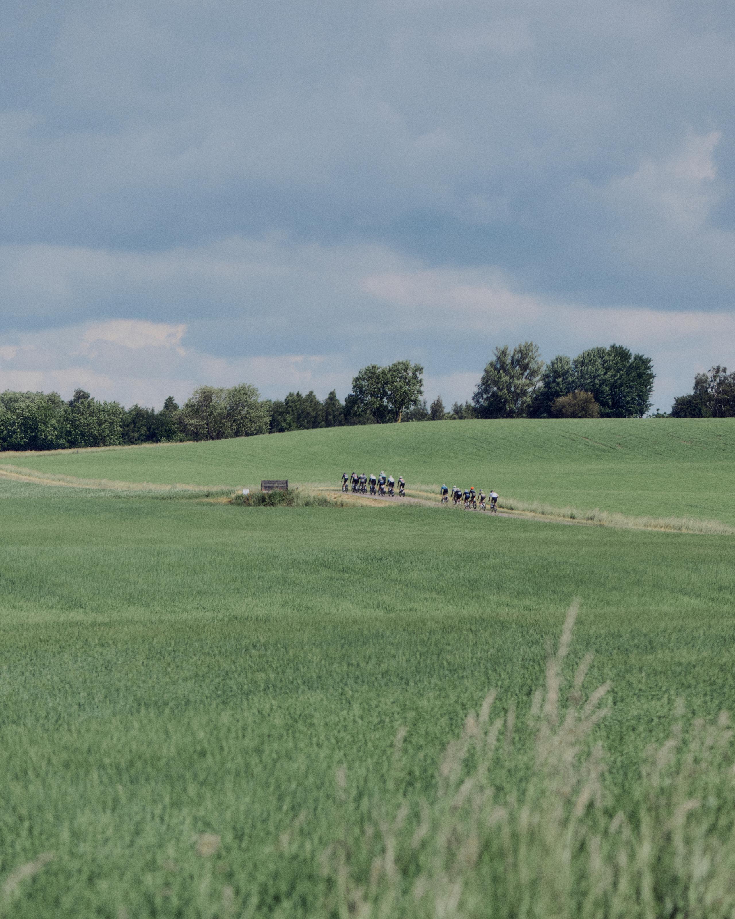 Cycling group riding through green countryside fields under cloudy sky