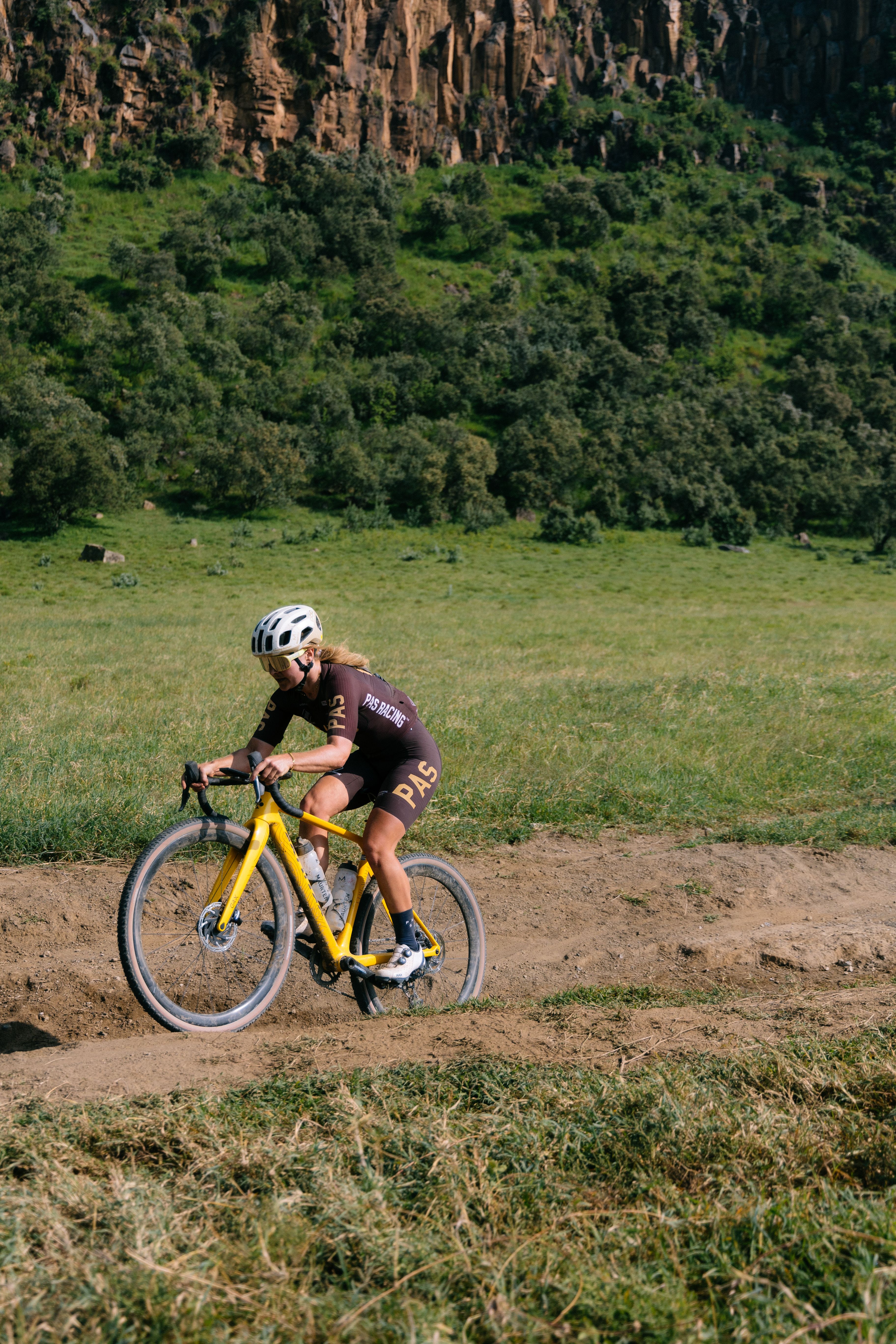 Model wearing brown gravel cycling outfit on yellow bike in countryside field setting