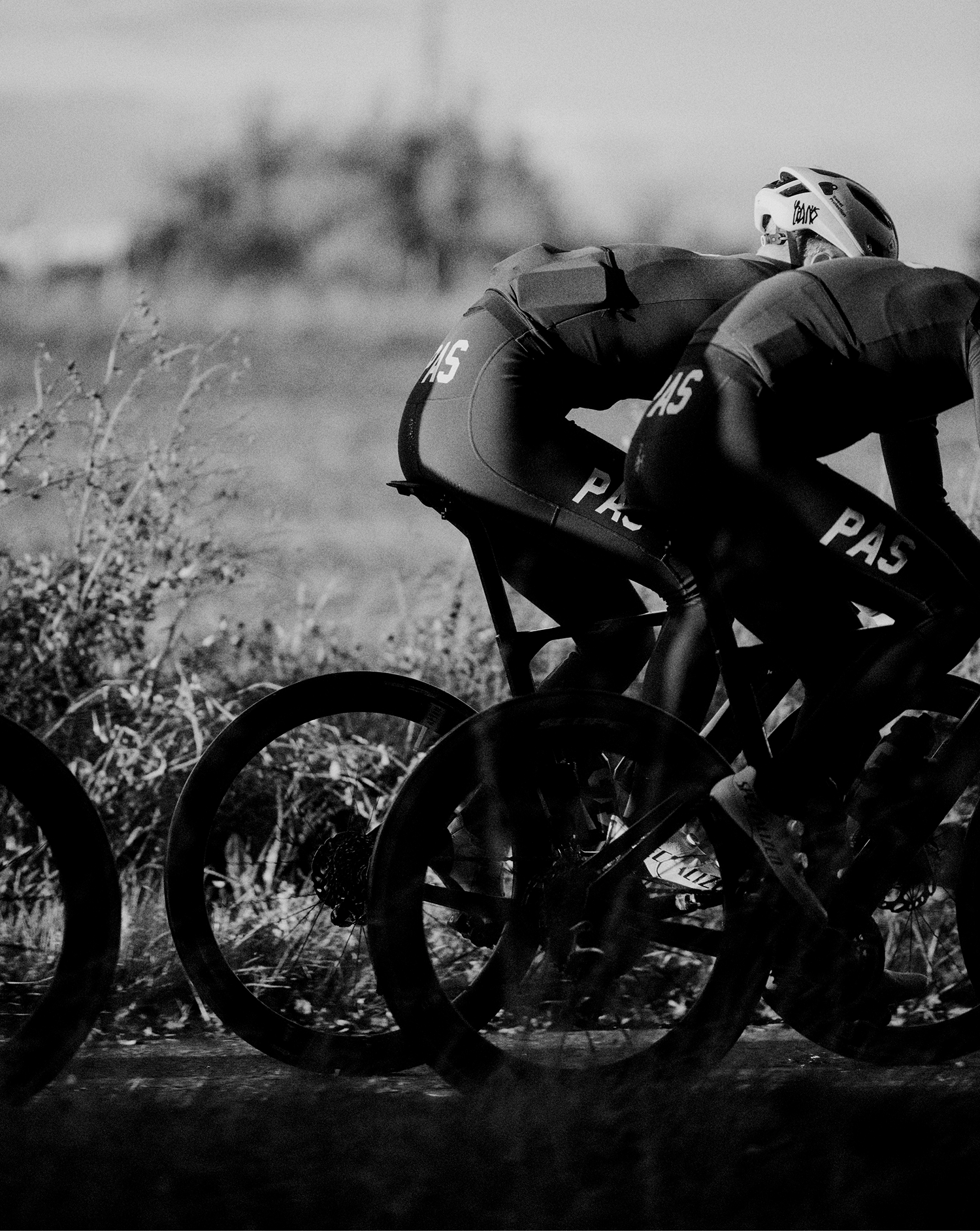 Two cyclists in aerodynamic position wearing PAS collection cycling apparel in black and white photograph