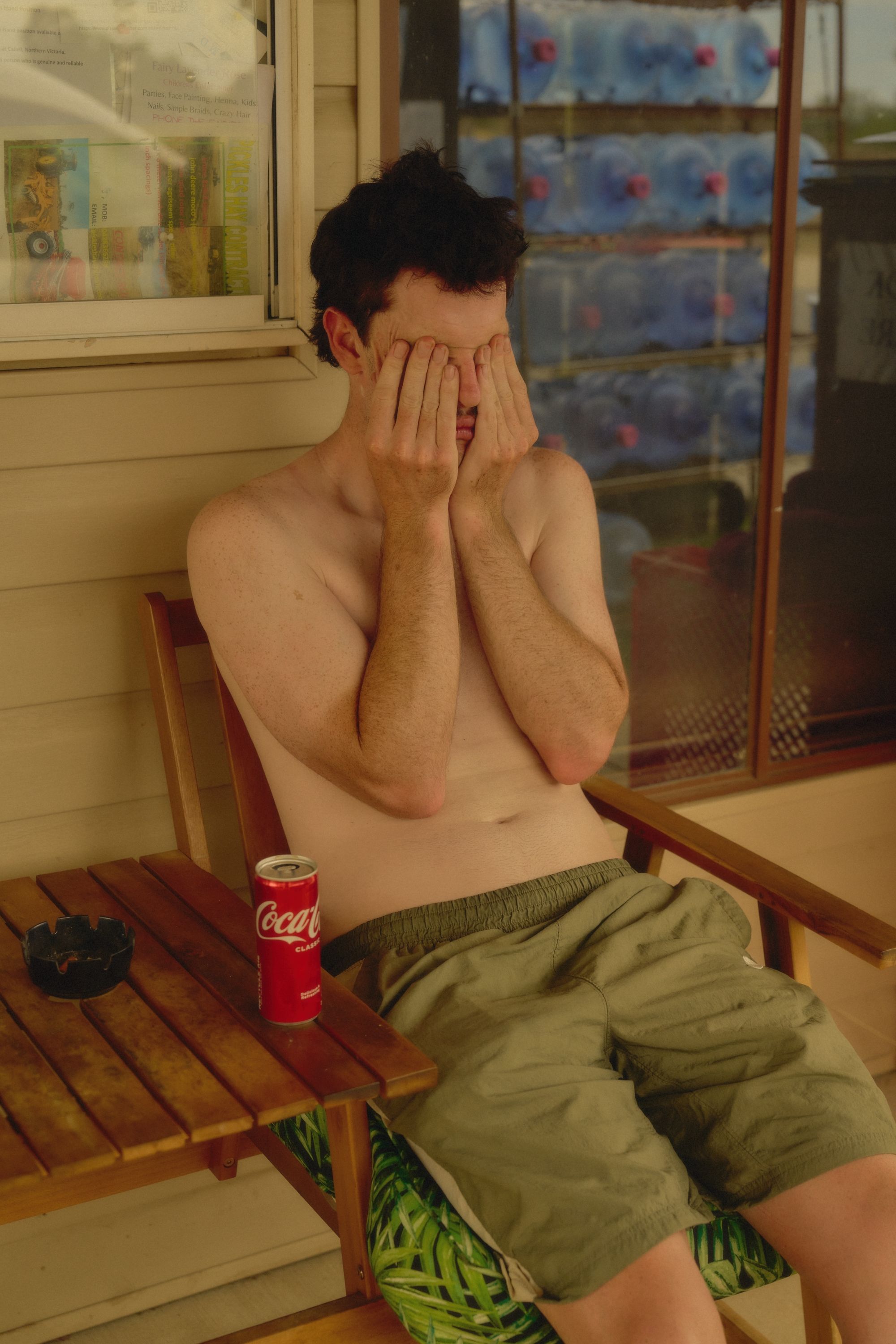 Model with hands covering face wearing green shorts, seated on wooden bench