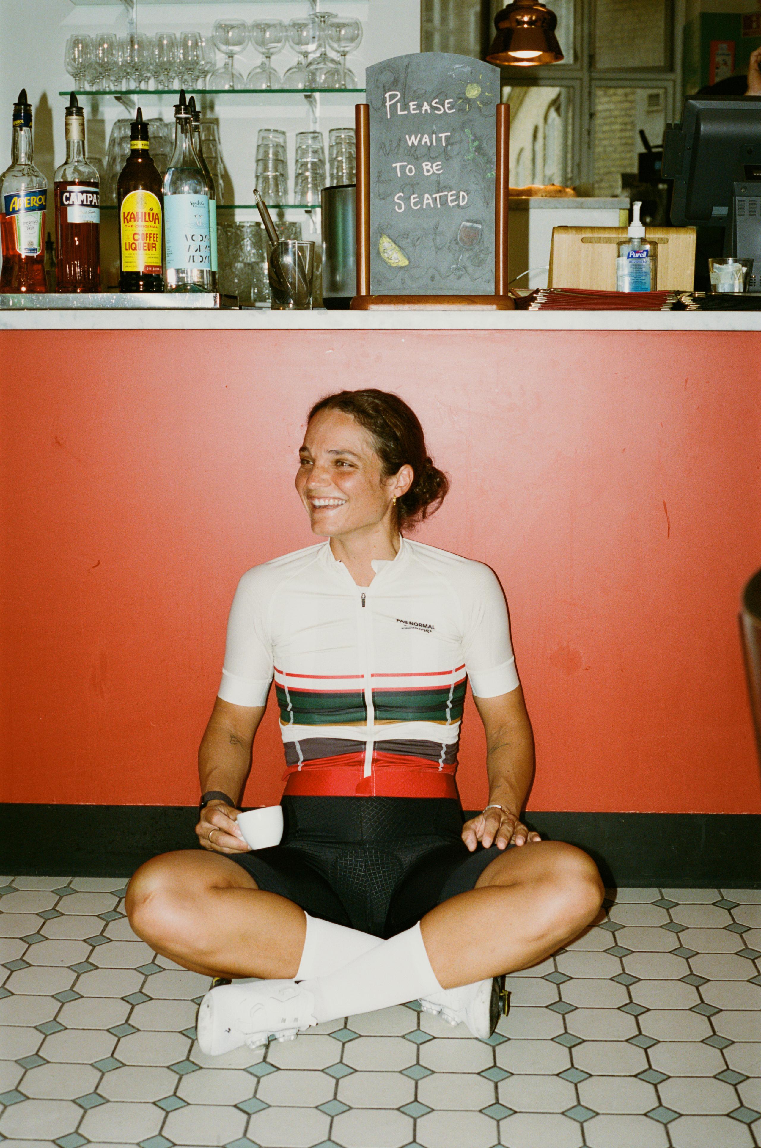 Model wearing Women's Mechanism jersey with horizontal stripes in white, green, and red, seated in cafe