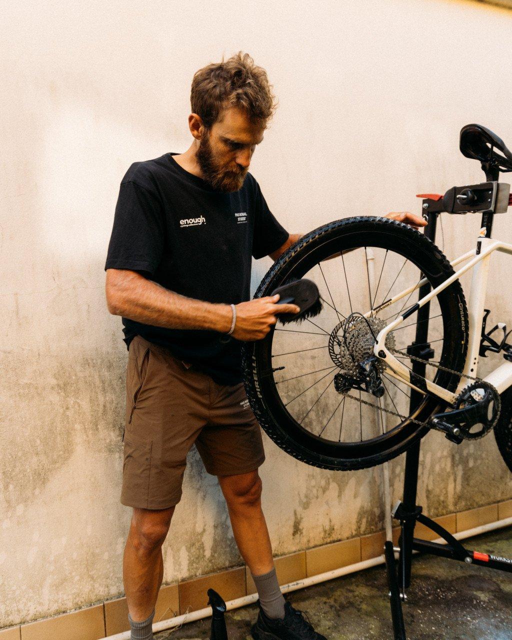 Model wearing black t-shirt with chest lettering while maintaining bicycle wheel in bike stand