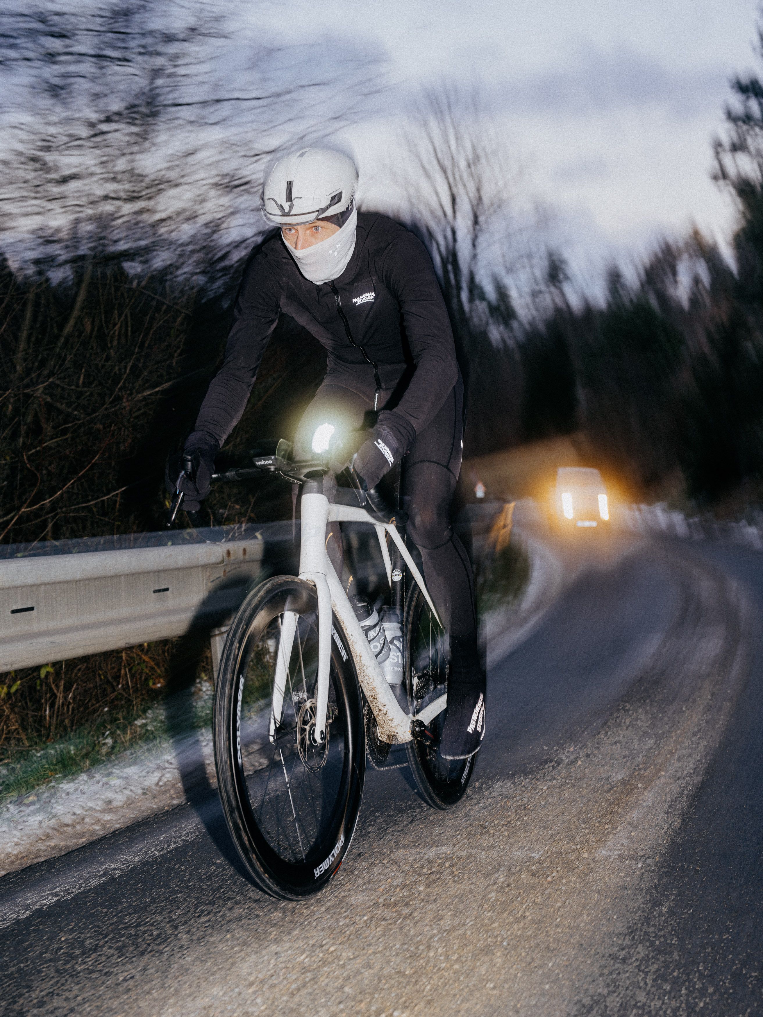 Model wearing black cycling apparel and white helmet on time trial bike during evening ride on country road