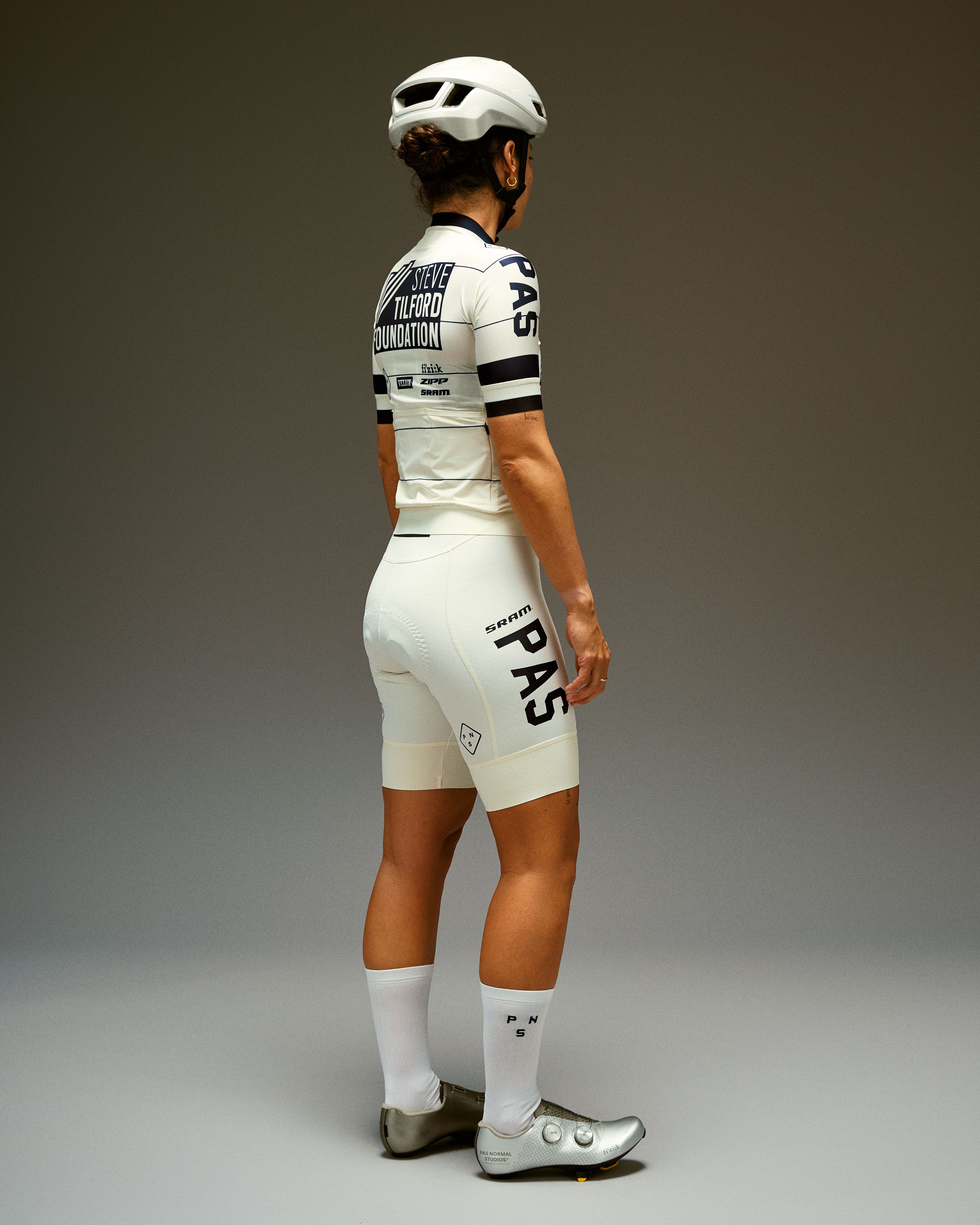 Model wearing white cycling kit with black accents, viewed from behind in studio setting