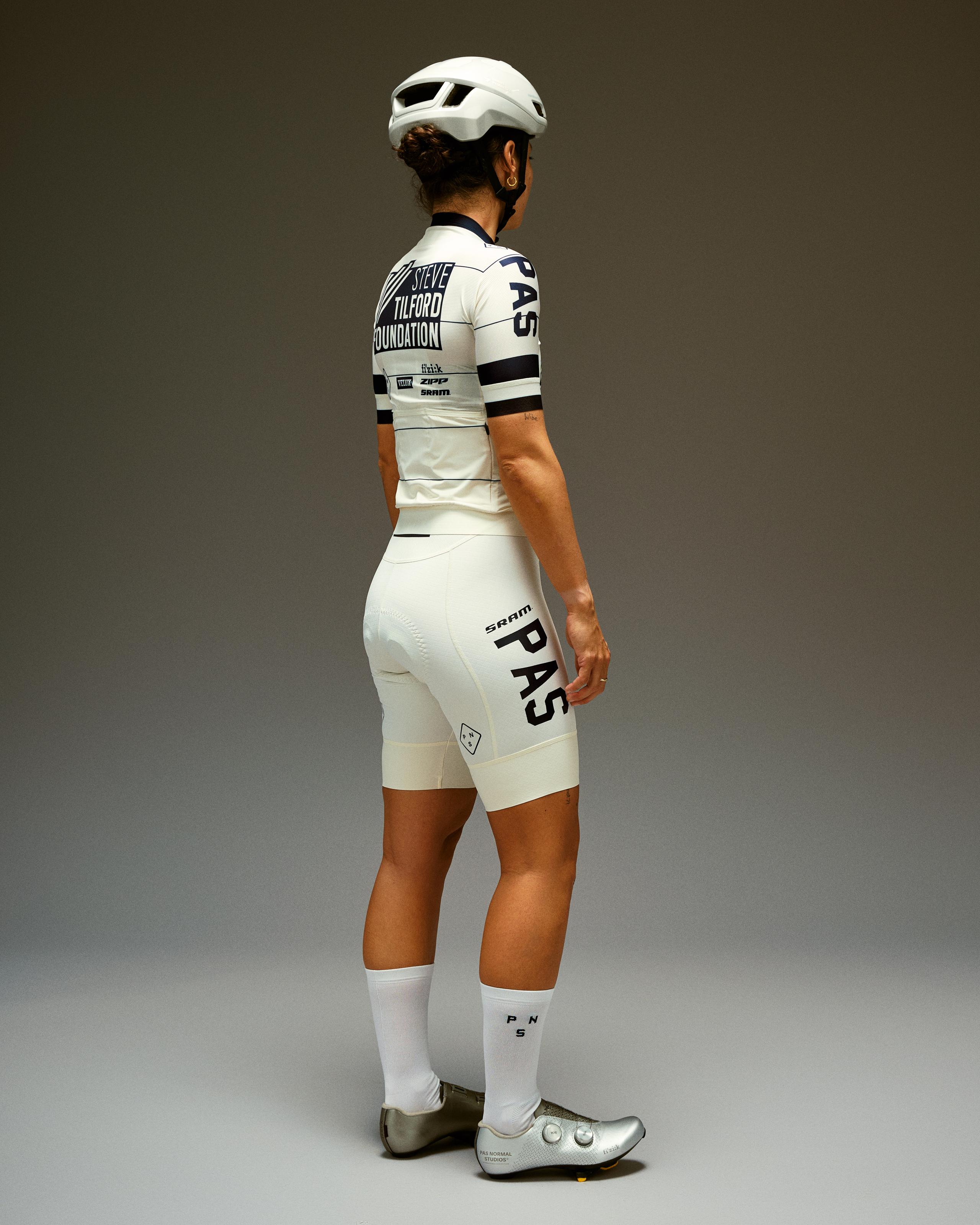 Model wearing white cycling kit with black accents, viewed from behind in studio setting