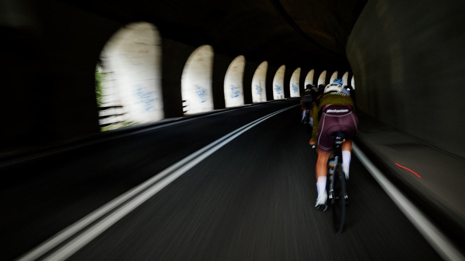Cyclist in purple jersey riding through tunnel with arched windows
