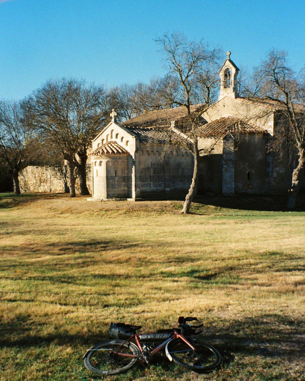 Bicycle with orange frame resting on grass in front of historic stone church with bell tower
