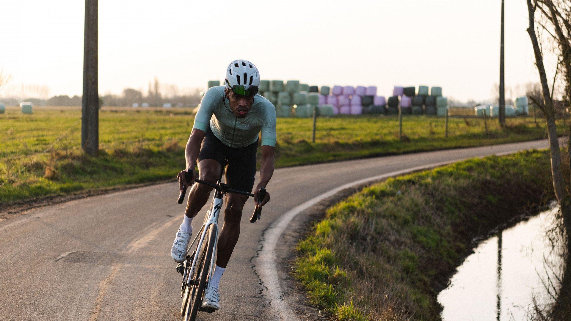 Model wearing light green cycling jersey in time trial position on country road at golden hour