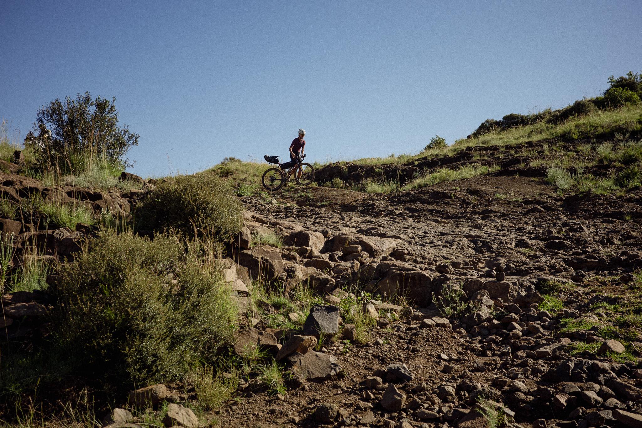 Model wearing cycling apparel on rocky mountain terrain in Lesotho with gravel bike