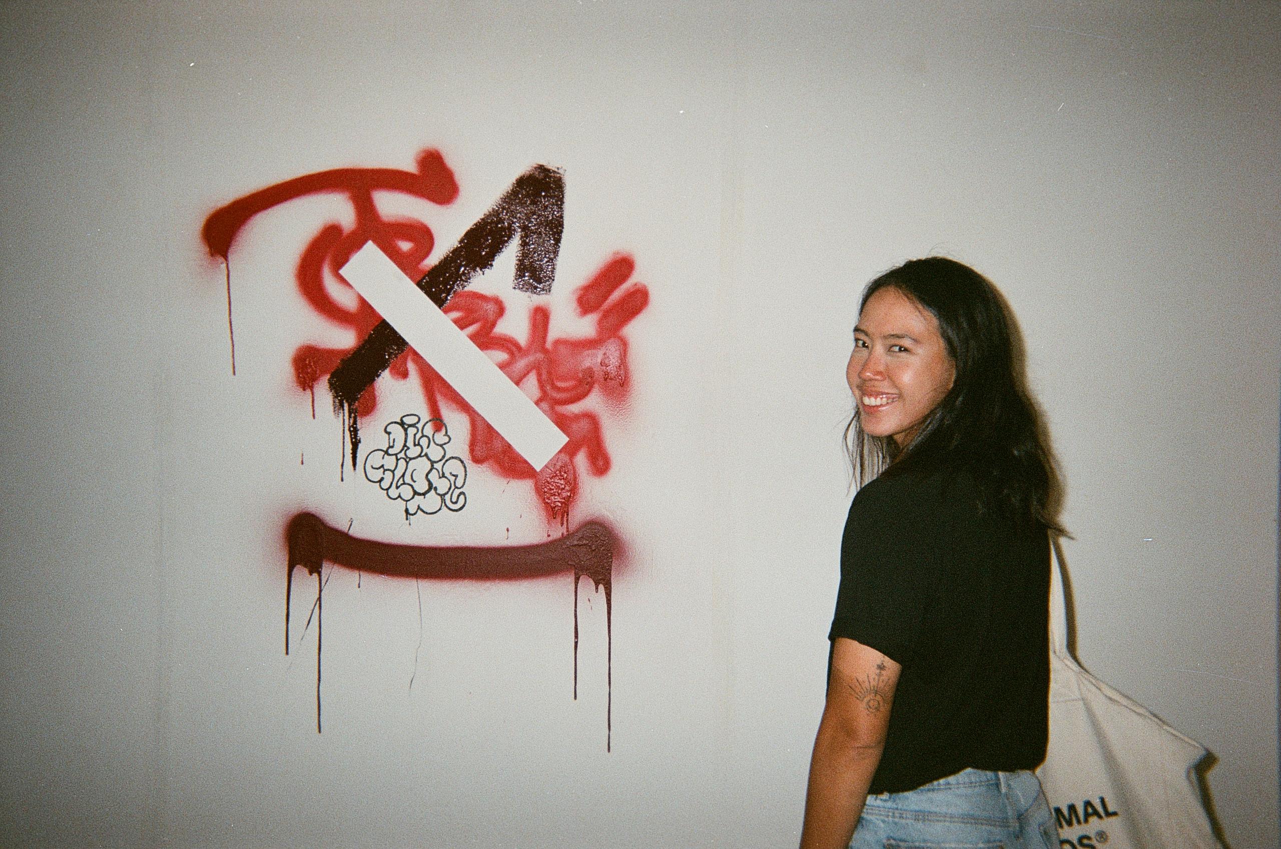Model wearing black top standing next to graffiti art on white wall