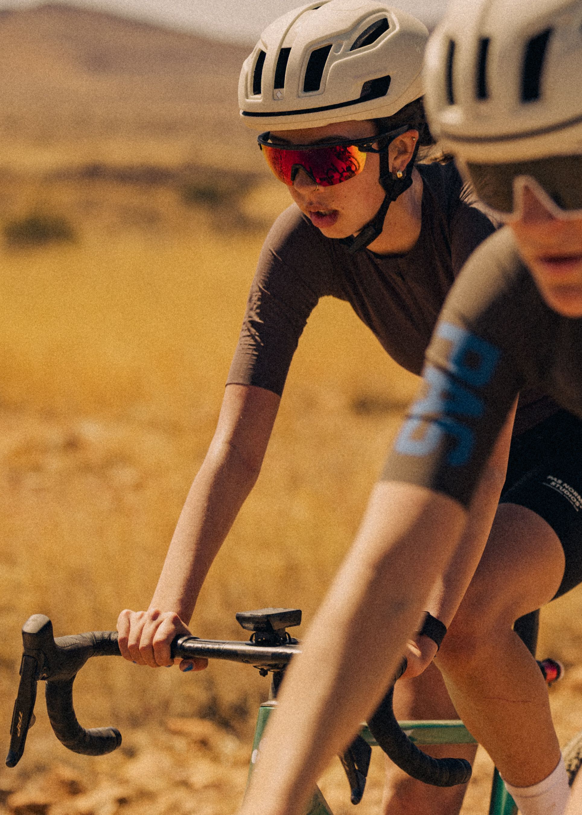 Model wearing black cycling jersey in aerodynamic position on time trial bike in desert setting