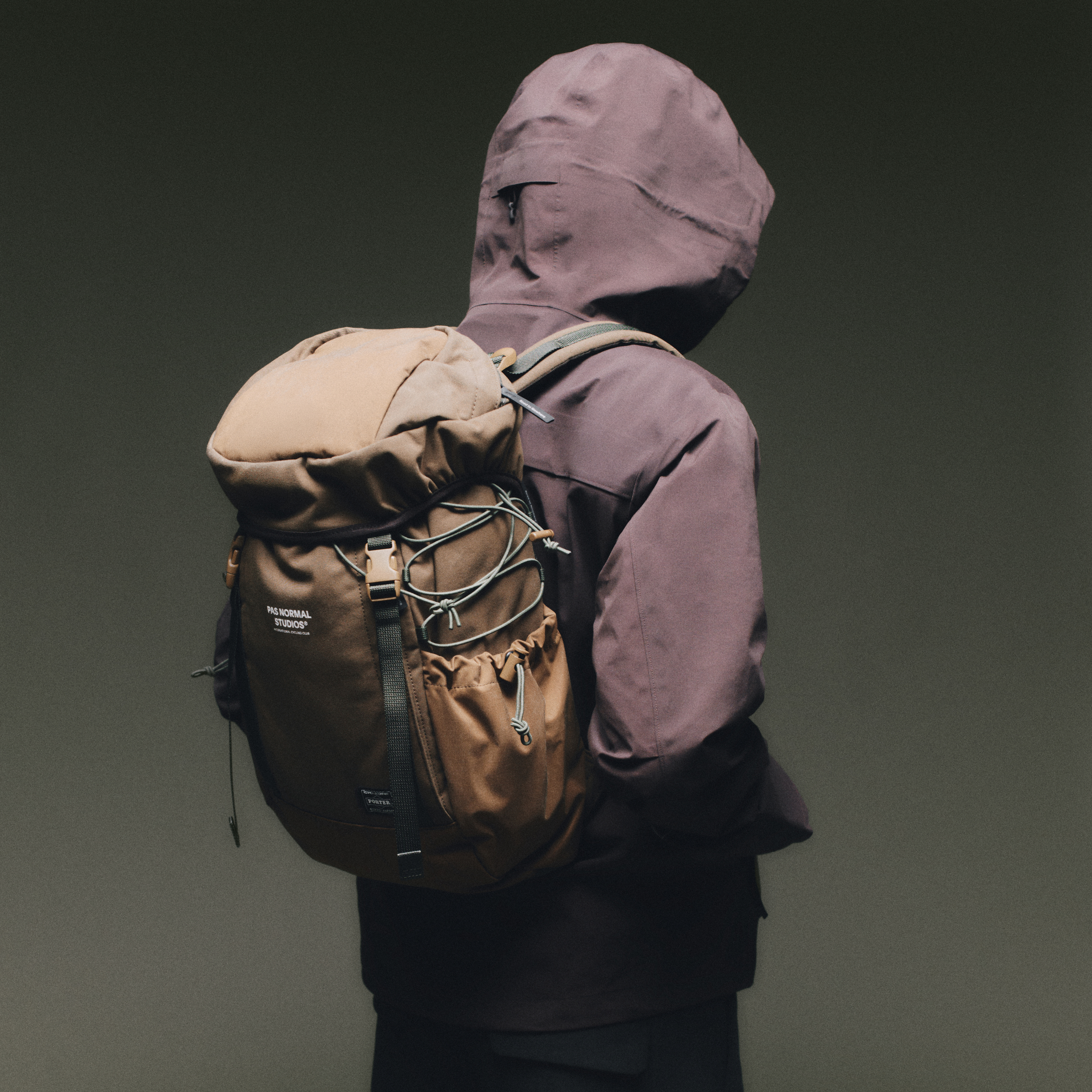 Tan Porter-Yoshida backpack worn on model, rear view with roll-top closure and bungee cord front panel