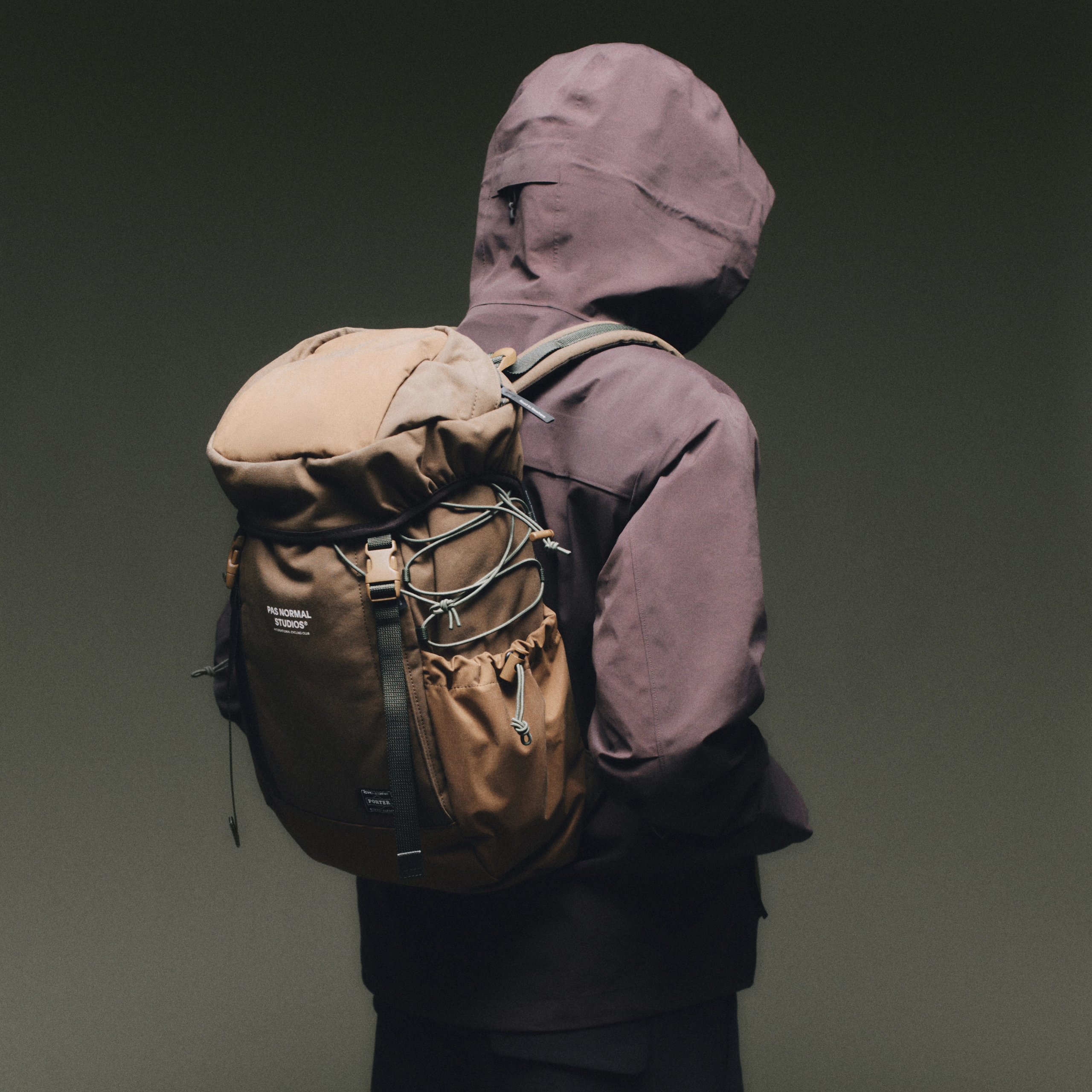 Tan Porter-Yoshida backpack worn on model, rear view with roll-top closure and bungee cord front panel