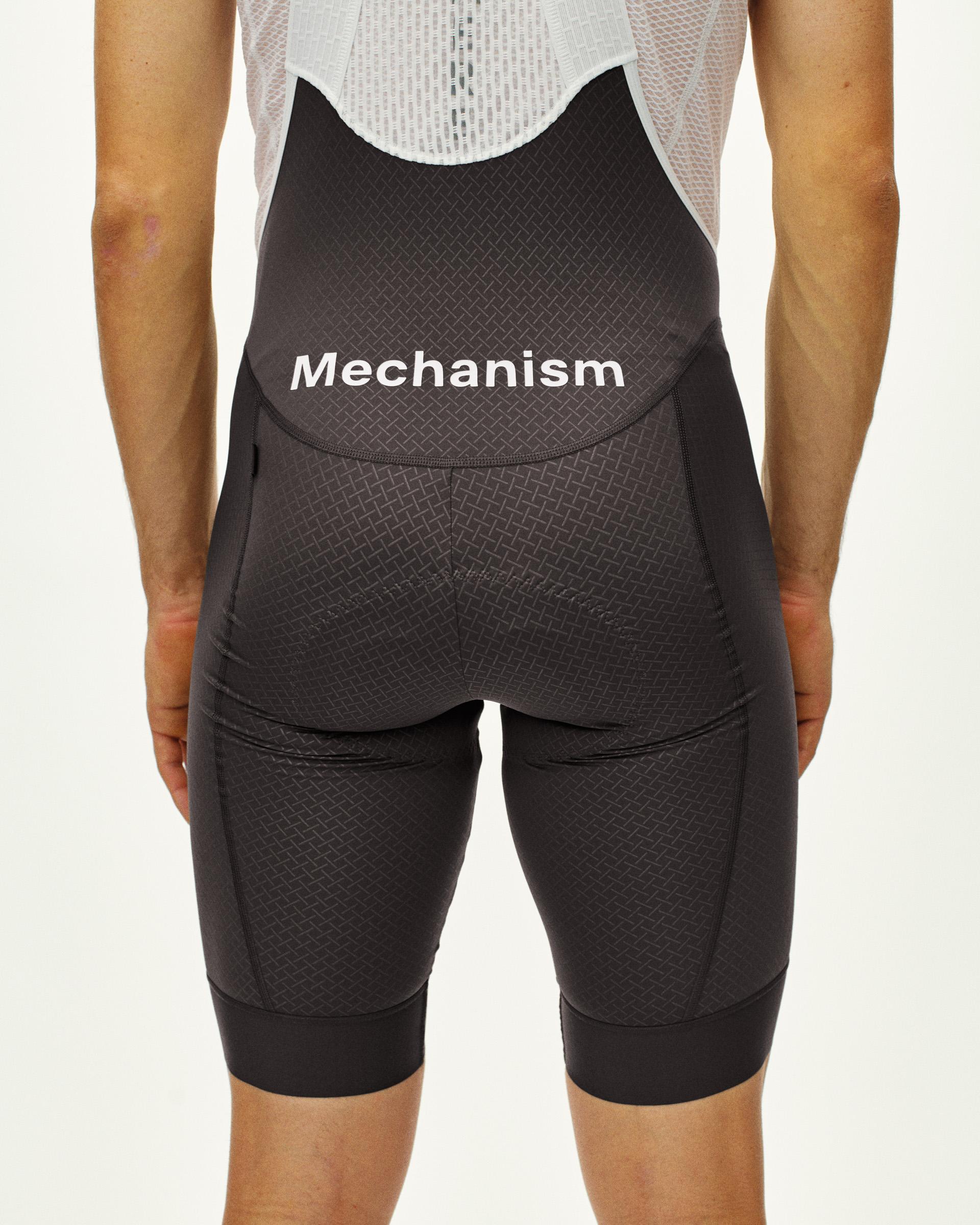 Dark Grey Mechanism cycling bibs on model, rear view with white logo print and textured fabric panels