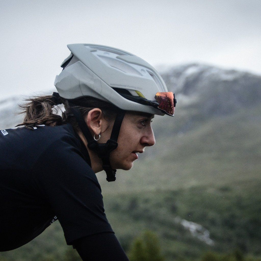 Model wearing white aerodynamic cycling helmet with tinted visor in mountain landscape