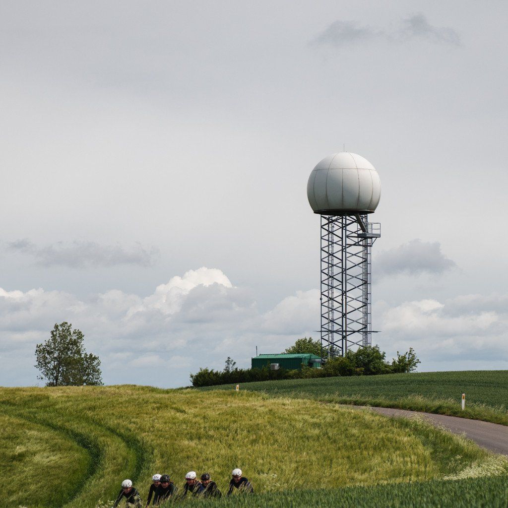 Cyclists in aerodynamic position racing past radar tower in rural countryside