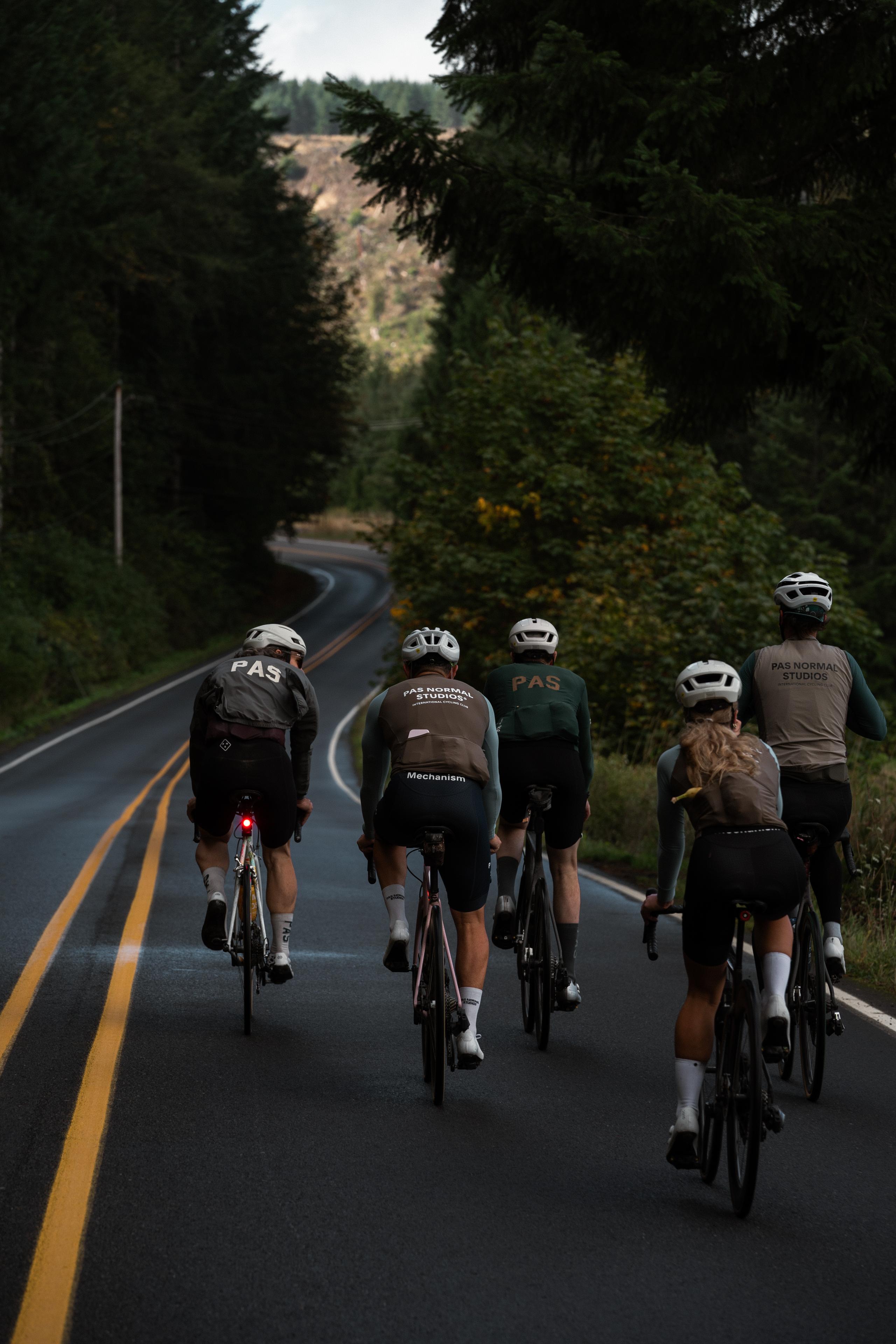 Group of cyclists riding on forest road wearing PAS collection jerseys and shorts in various earth tones