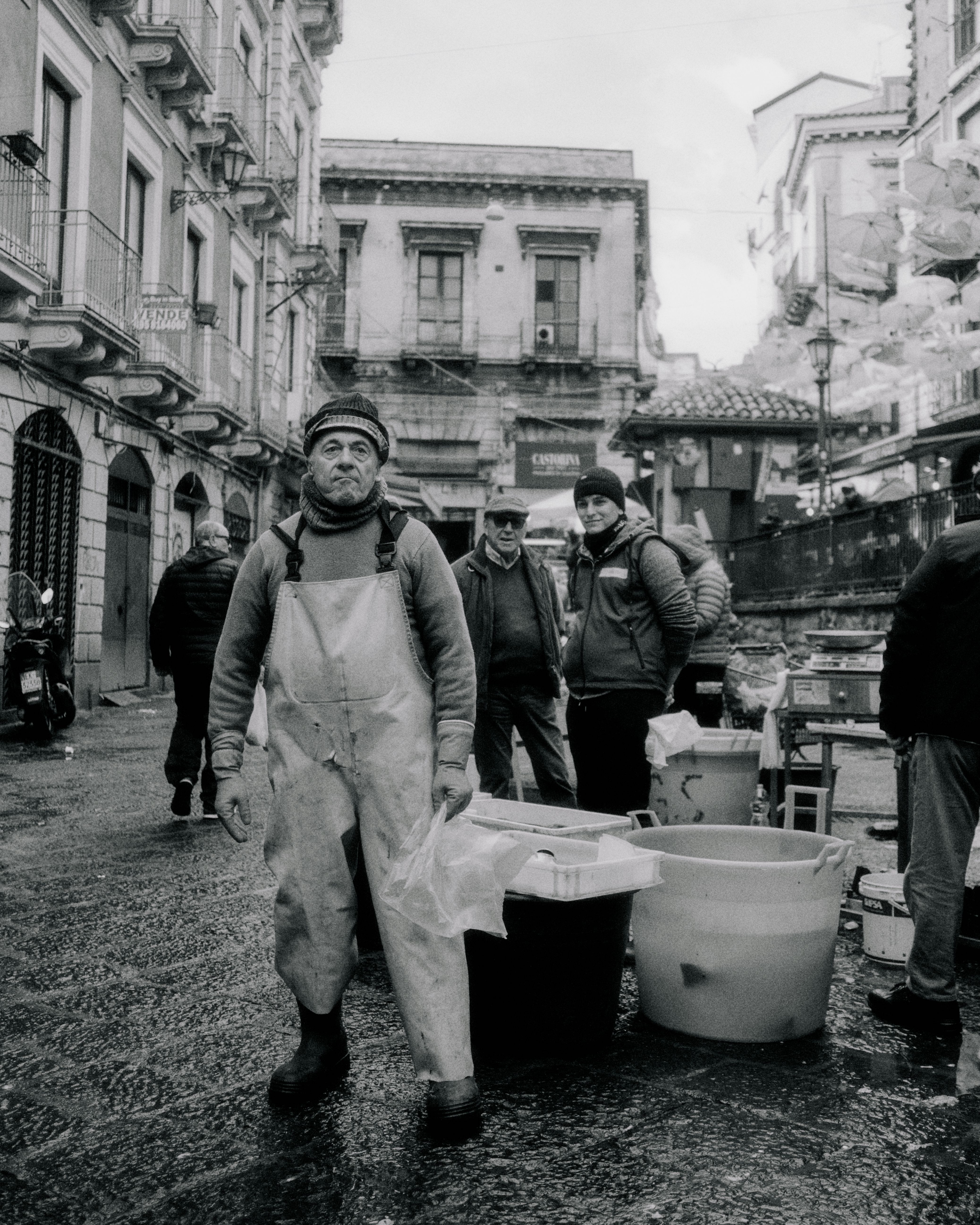 Black and white photo of fishermen at outdoor market in Sicily with traditional architecture