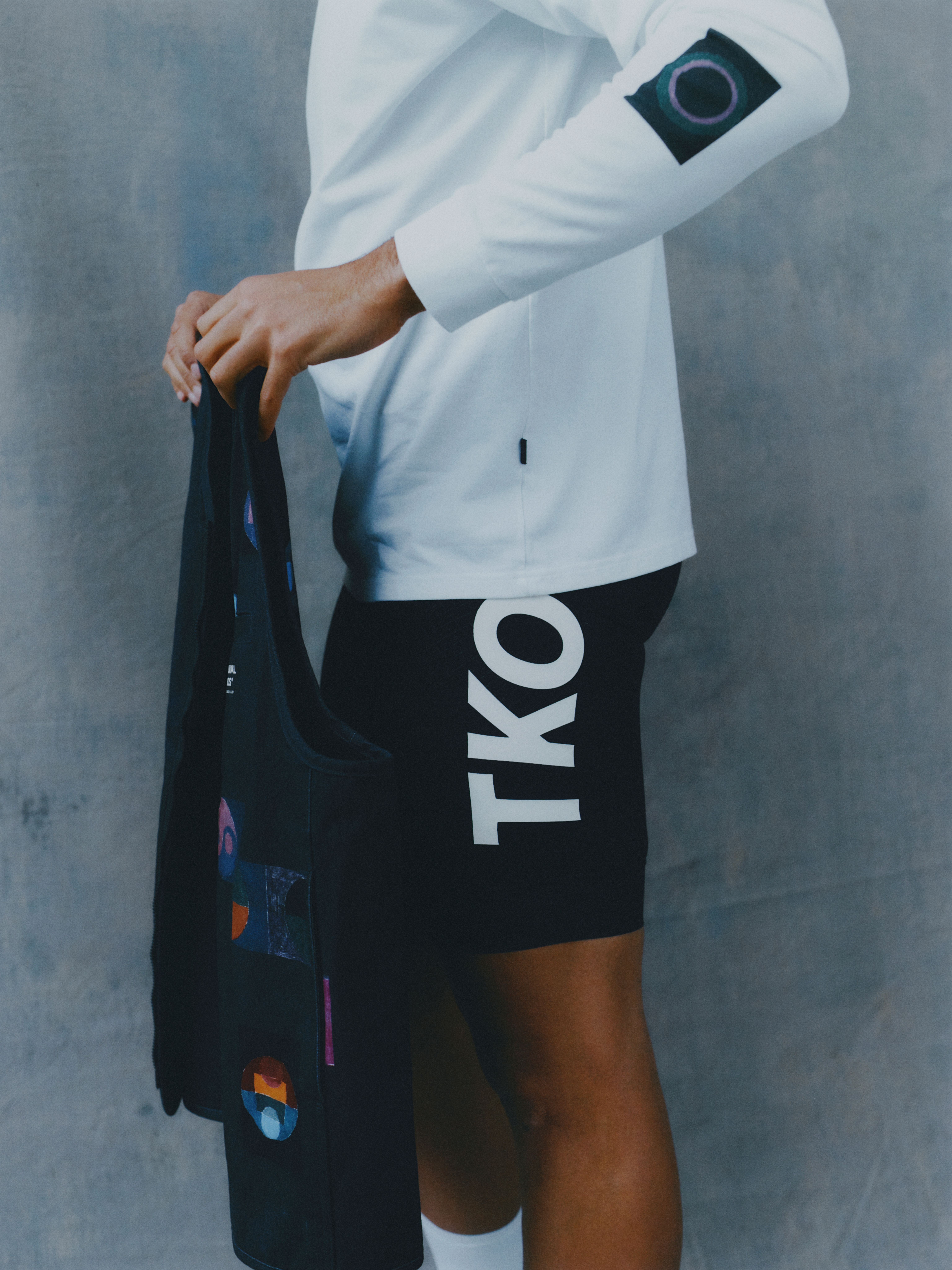 Model wearing white long sleeve jersey and black shorts with colorful graphic elements from T.K.O. collection