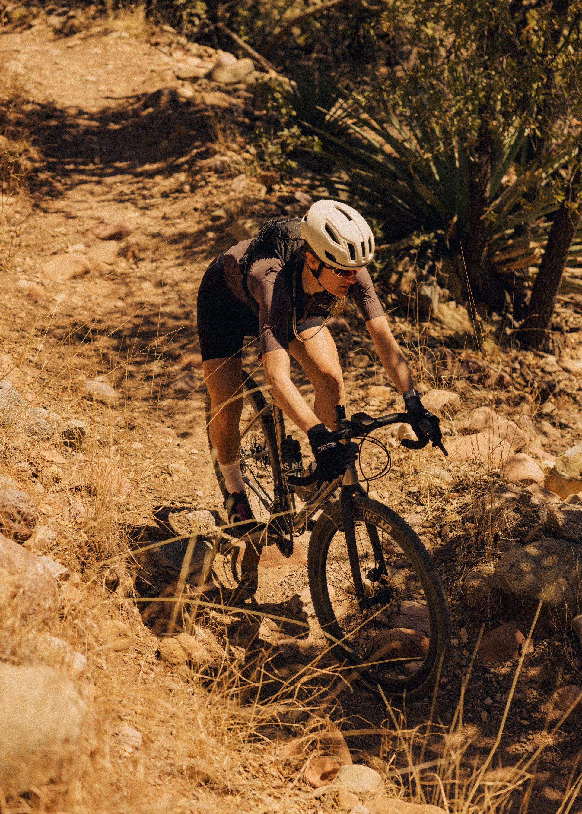 Model wearing brown cycling jersey and black shorts mountain biking on desert trail
