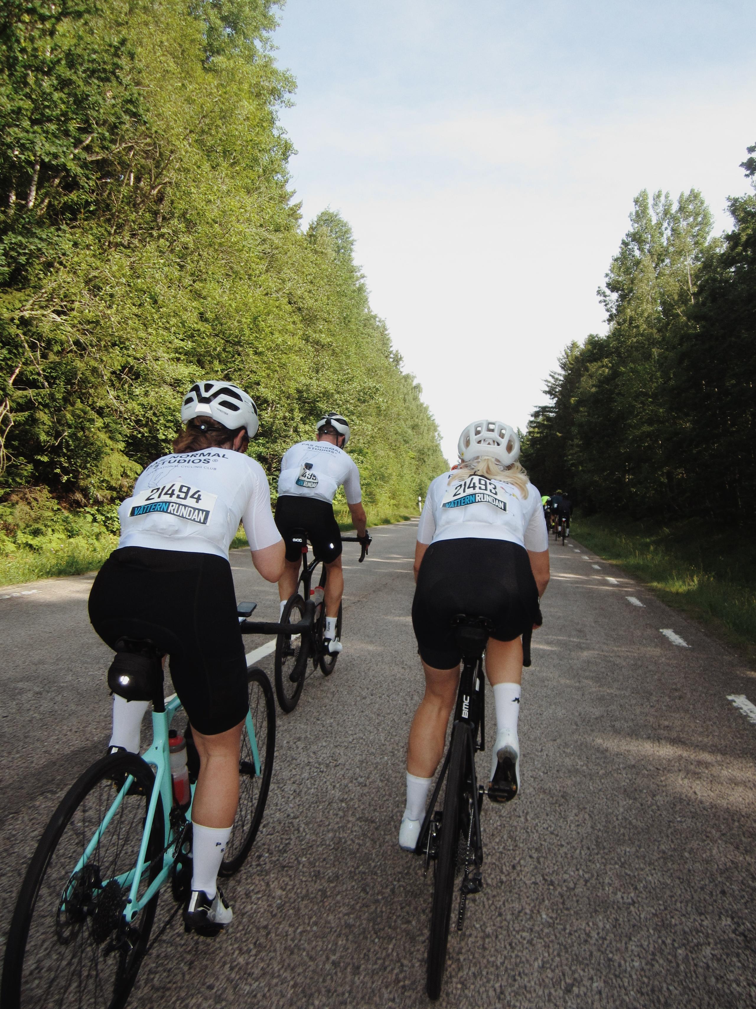 Cyclists wearing white jerseys with race numbers cycling on tree-lined road during Vätternrundan event