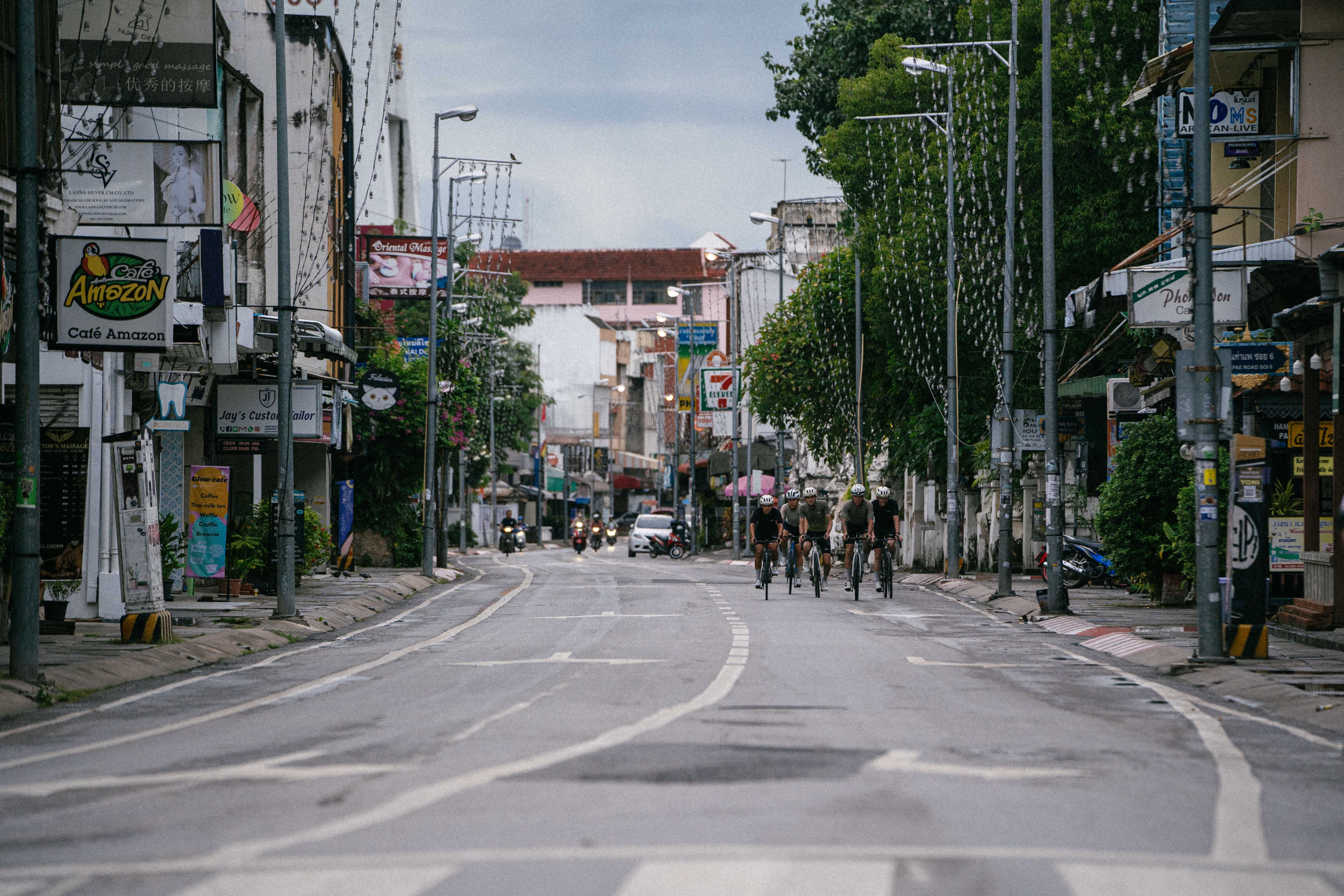 Group of cyclists riding through urban street in Thailand with shops and buildings on both sides