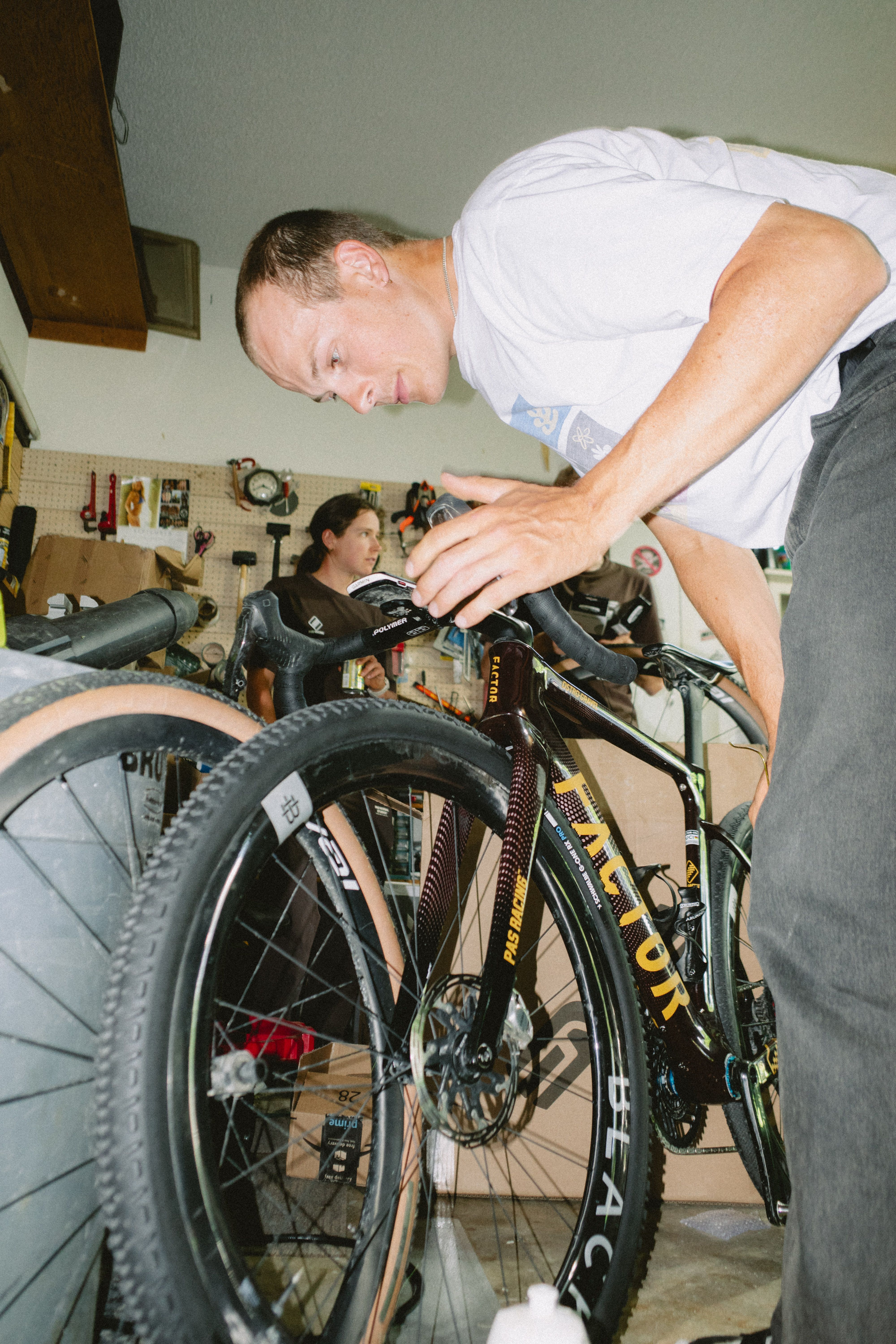 Man in white t-shirt adjusting mountain bike handlebars in workshop with woman in background