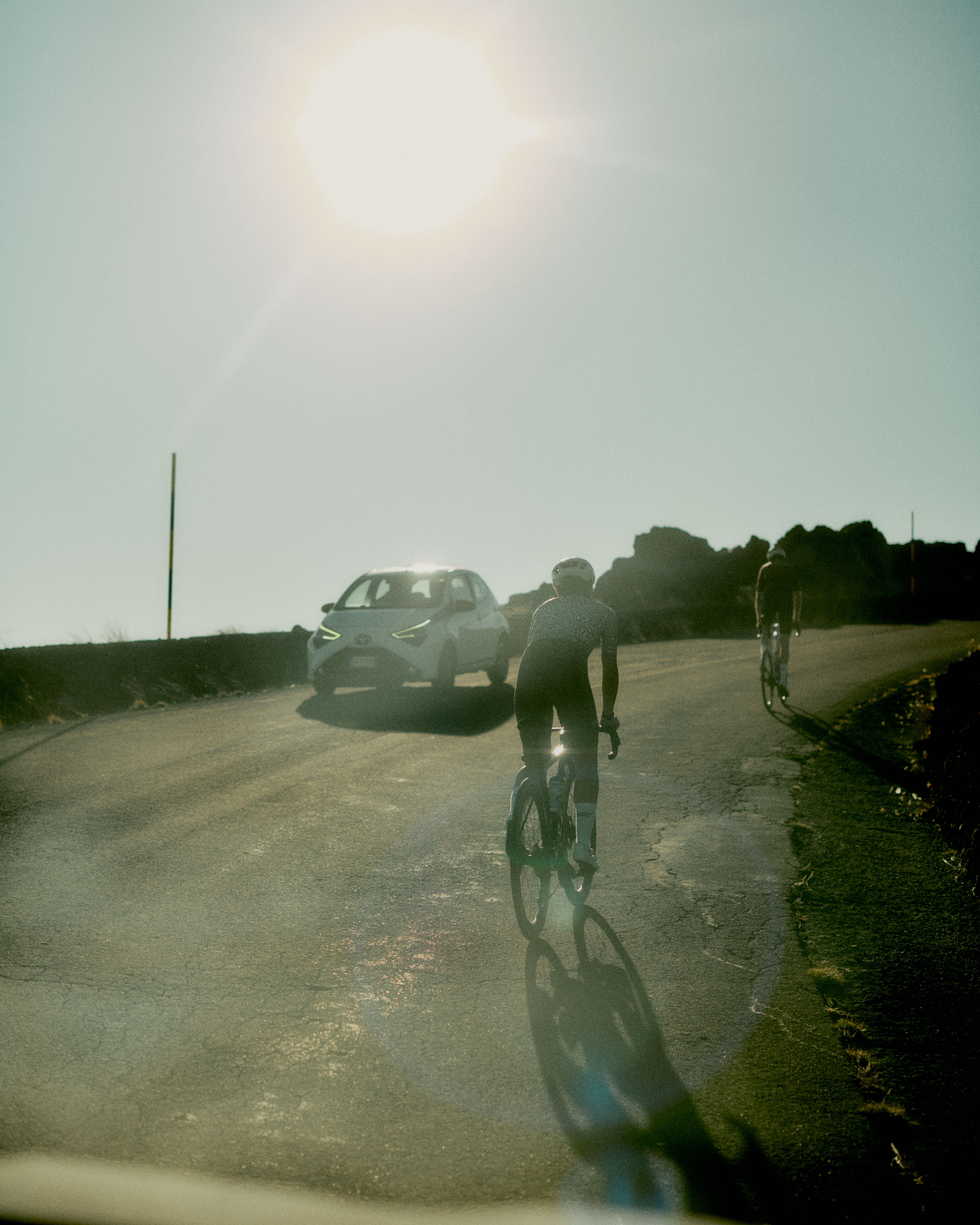 Cyclists on rural road with car support vehicle in Sicily