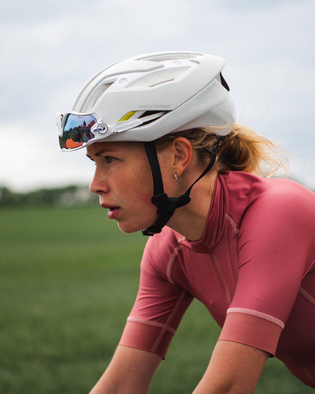 Model wearing pink jersey with white helmet and reflective visor in cycling position