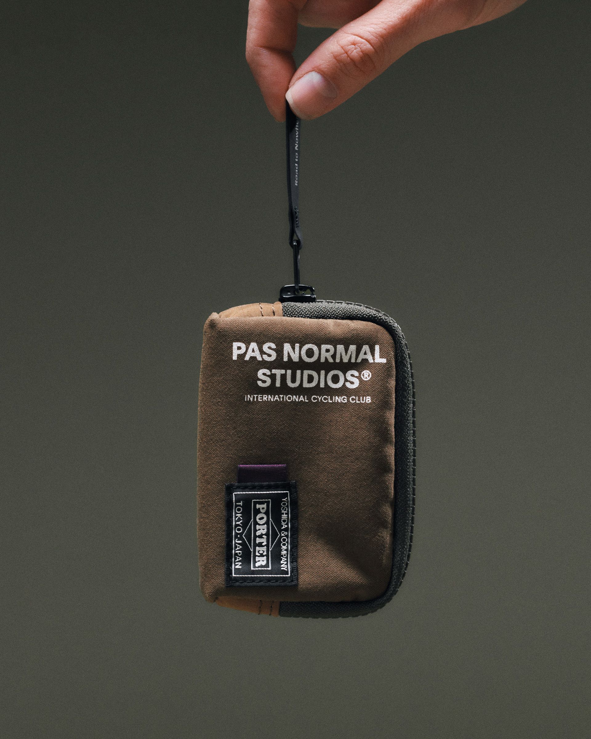 Light Brown Porter-Yoshida coin case held by hand, front view with white logo print and Porter woven patch