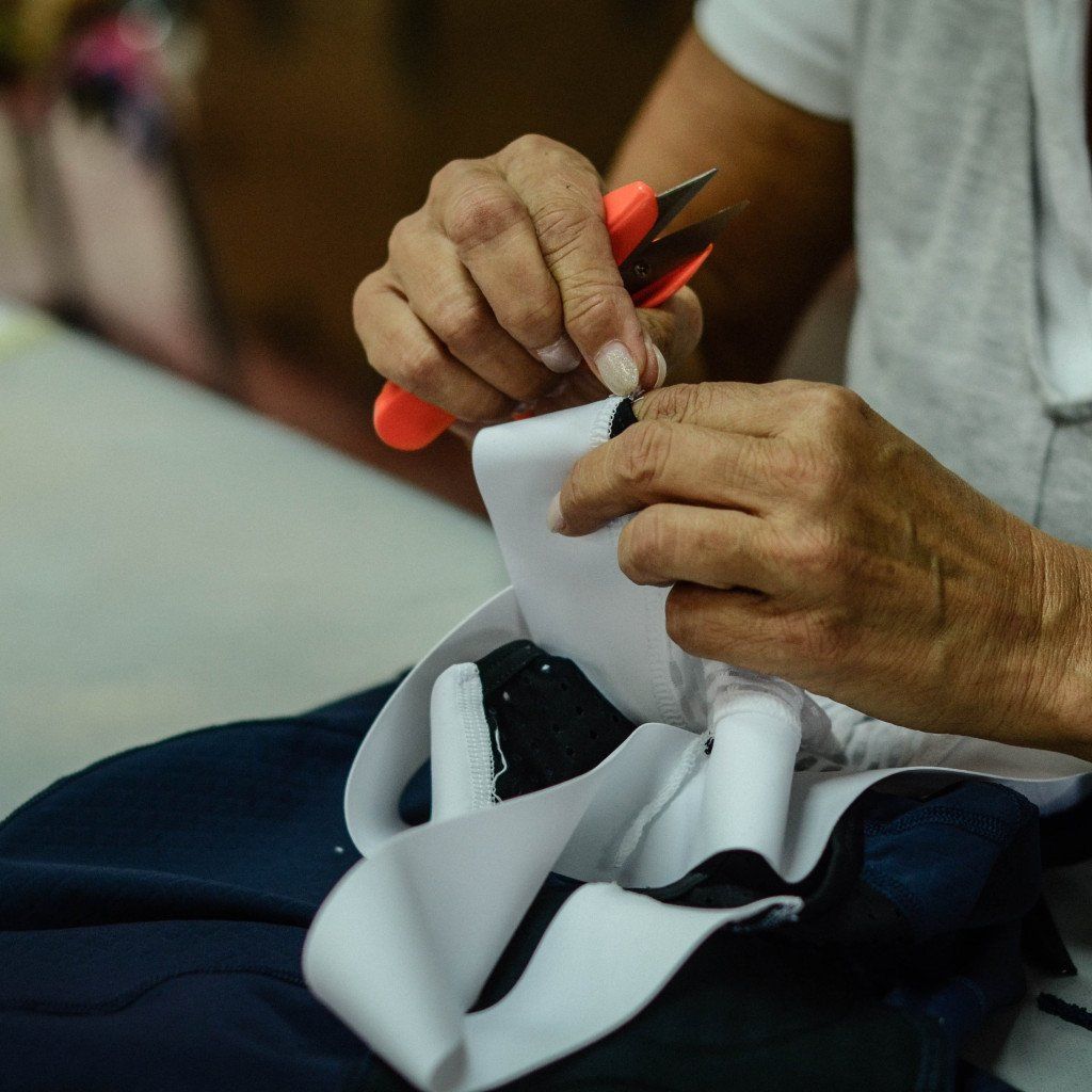 Hands cutting white ribbon with red-handled scissors above navy cycling apparel