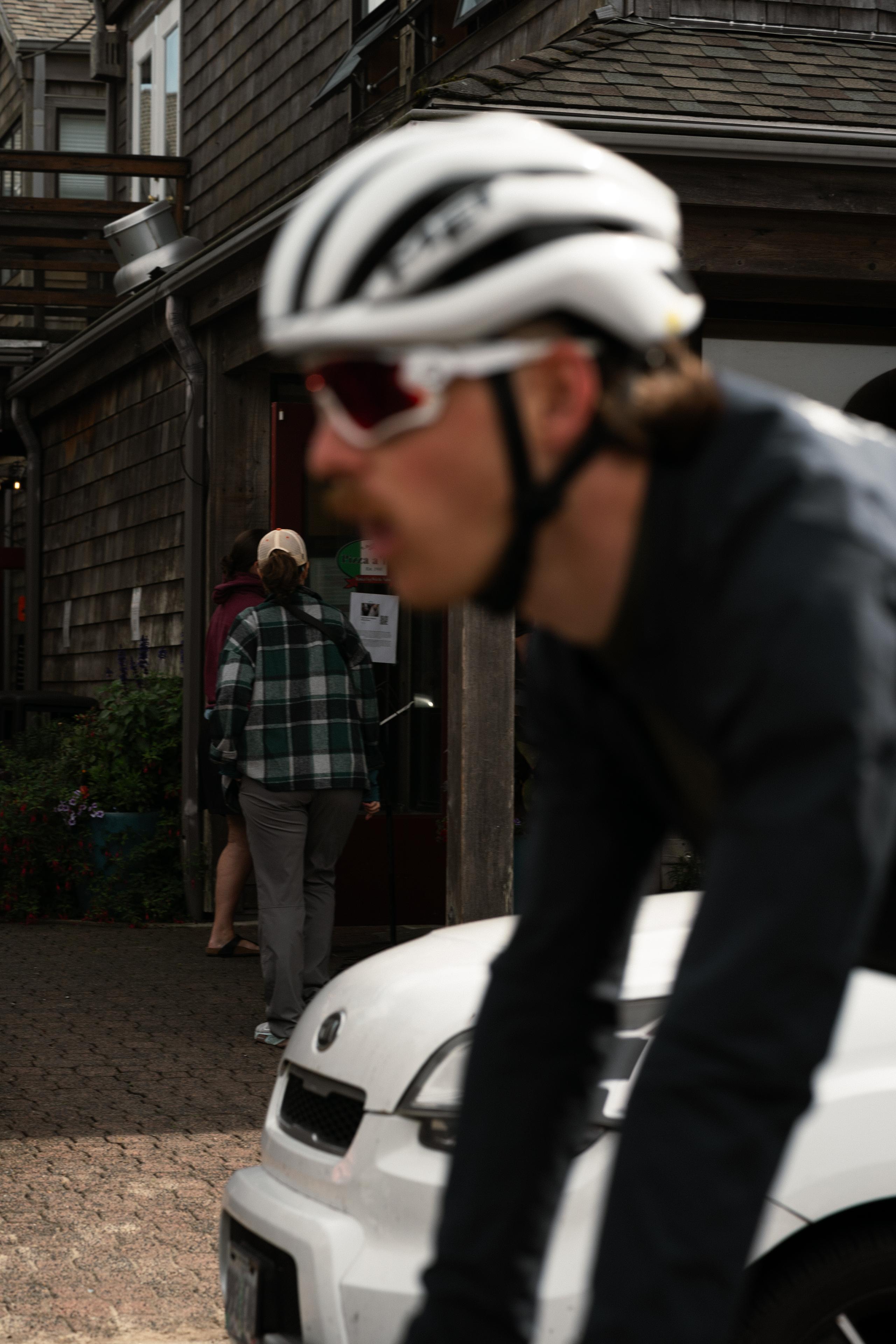 Cyclist in white helmet and dark jersey riding on street with pedestrian in background