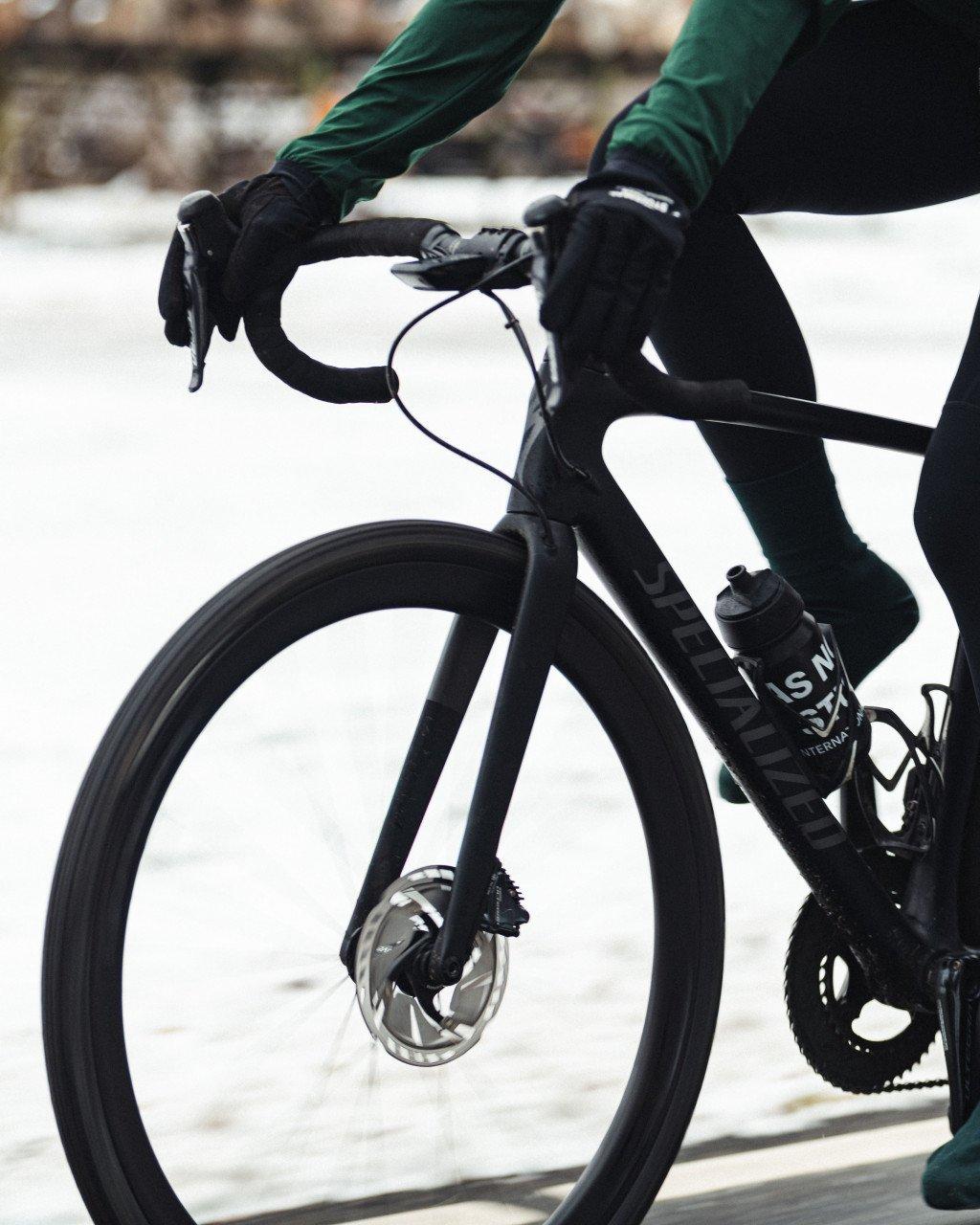 Cyclist in green jersey and black gloves on aerodynamic bike with disc wheel in winter setting