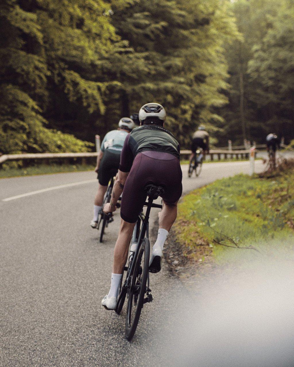 Cyclists in racing position on forest road, wearing burgundy and teal jerseys with white helmets