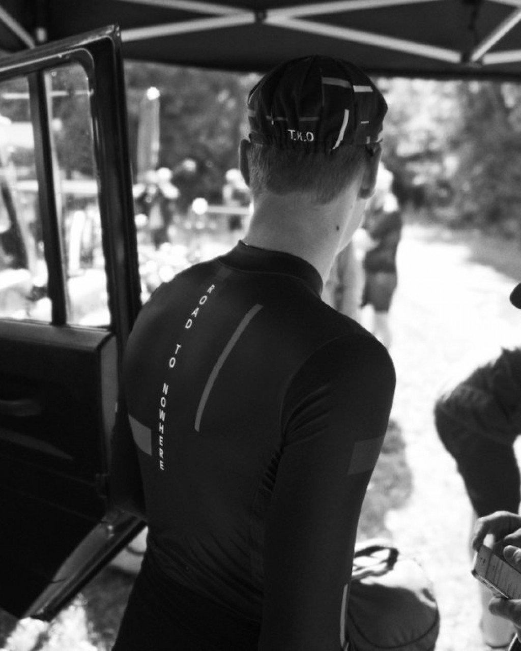 Model wearing black cycling jersey with back text panel, viewed from behind in vehicle